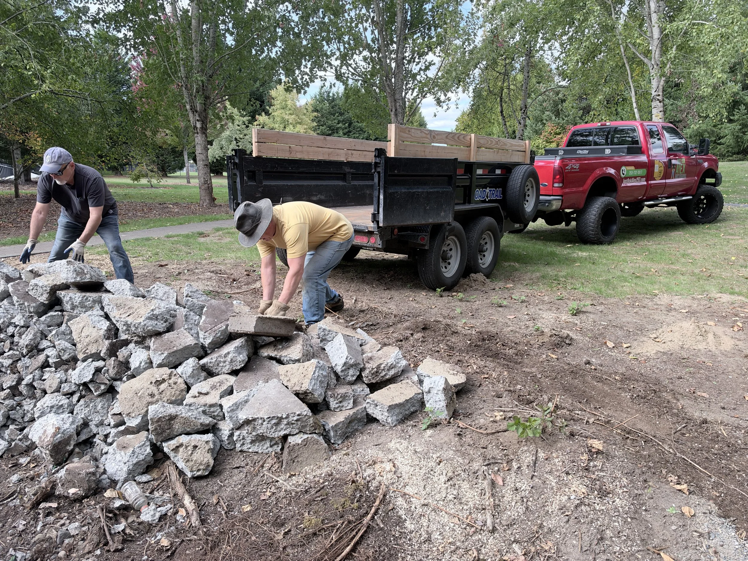 Just Ask Alex crew loading broken concrete by hand beside a red work truck and dump trailer at Sweetbriar HOA.