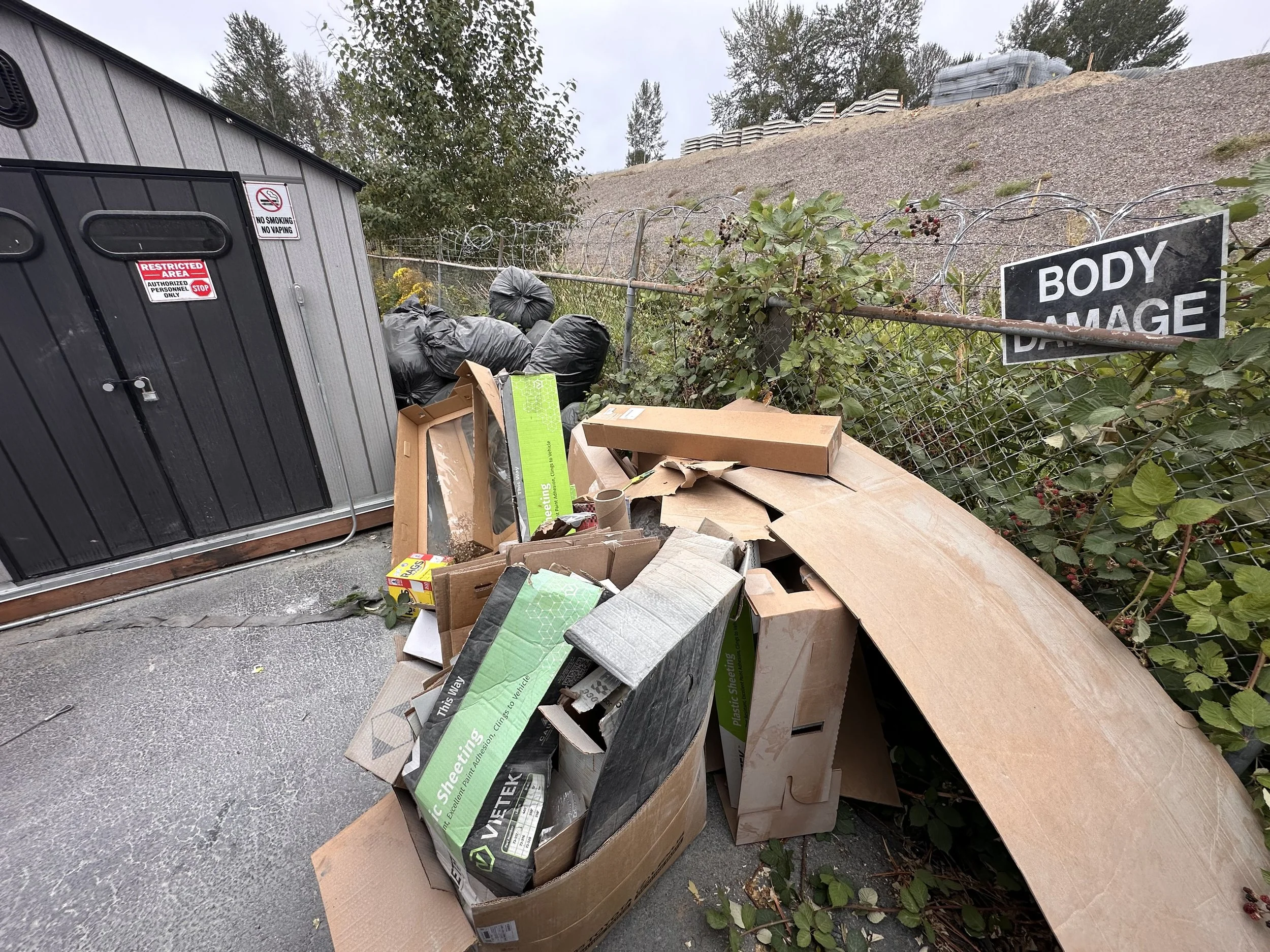 Pile of discarded cardboard, wood panels, packaging materials, and trash bags outside Dent Wizard in Burien, WA.