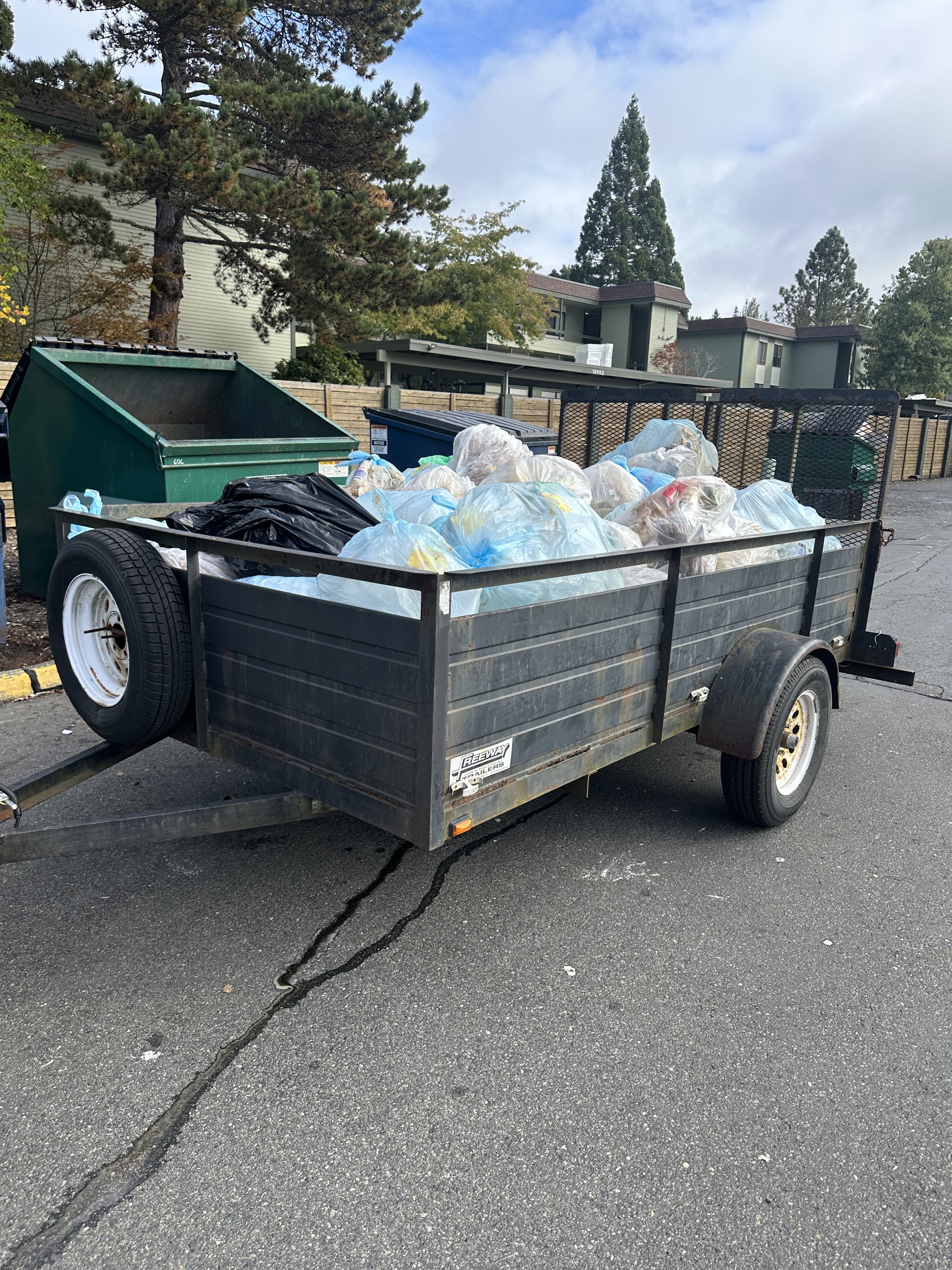 Trailer stacked with commercial center trash bags next to a dumpster enclosure in Seattle