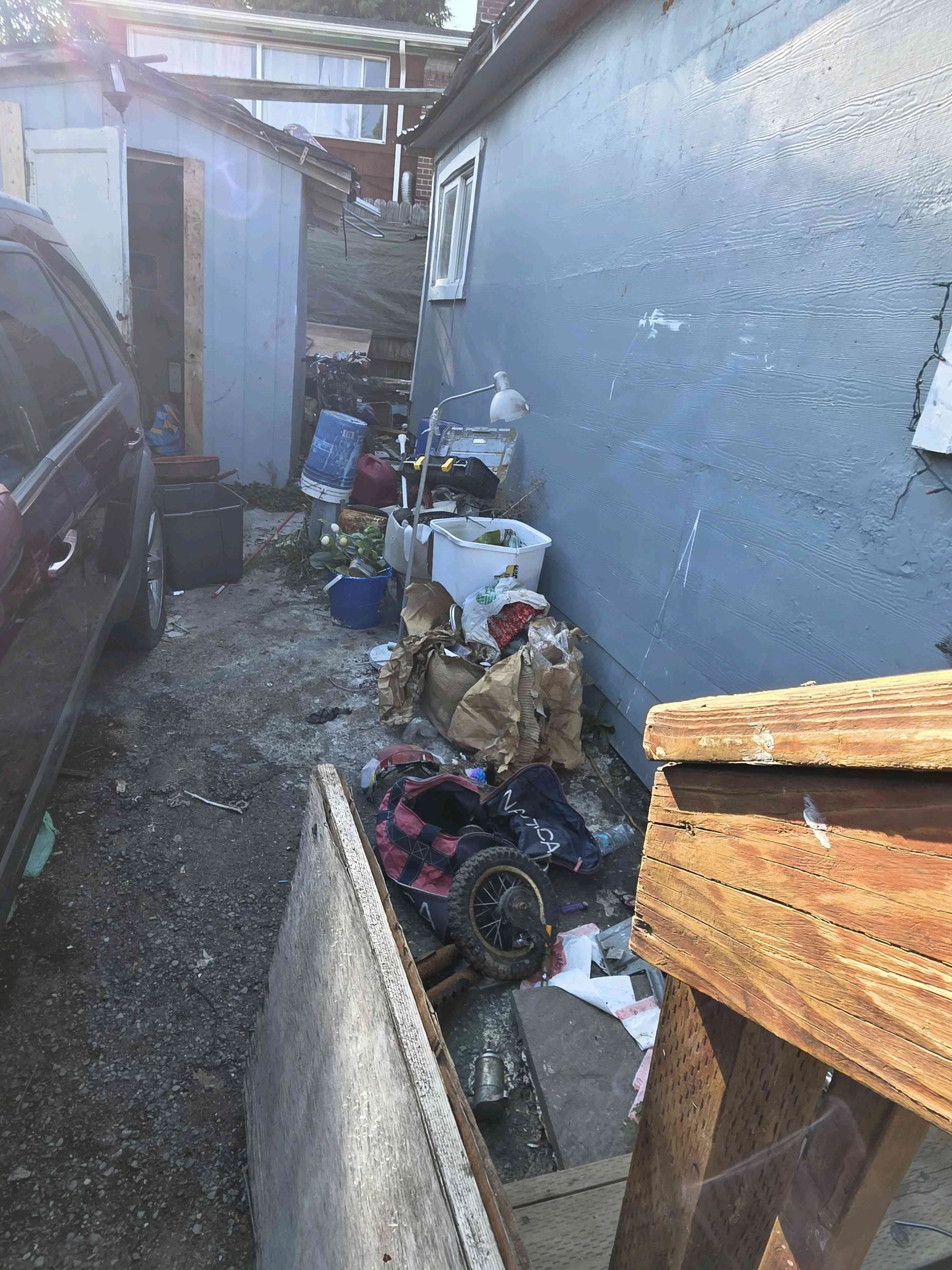 Discarded household items, bags, and miscellaneous debris alongside a residential building in Tukwila, King County.