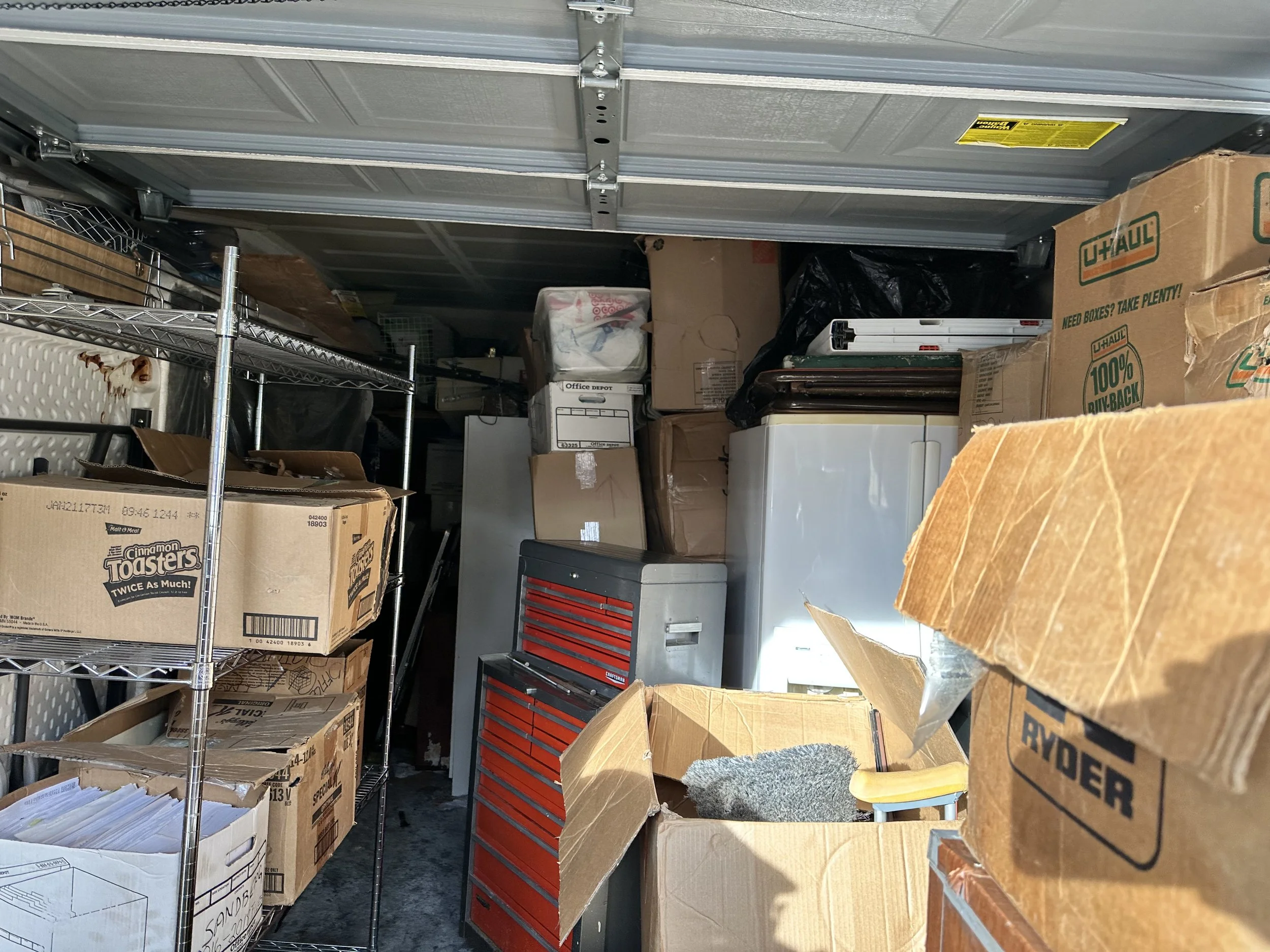 Inside view of an overfilled garage with boxes, shelving, and appliances staged for junk removal in Pierce County.