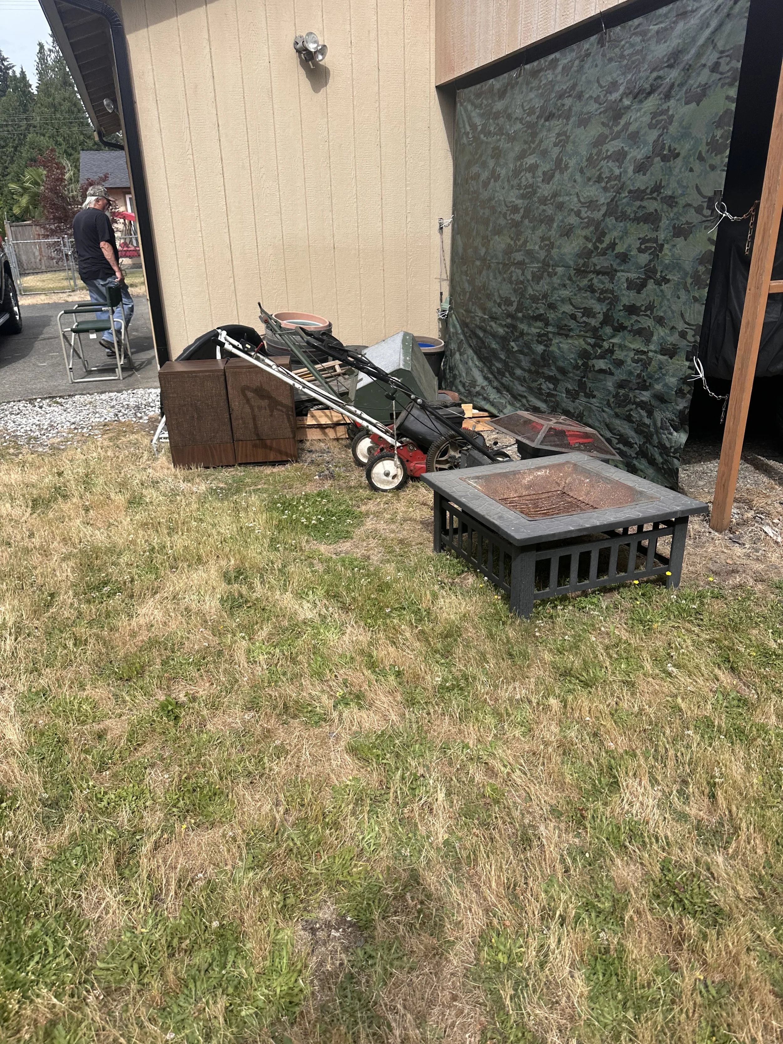 Old lawn mower, outdoor fire pit, and miscellaneous yard equipment beside a residential home before junk removal in Puyallup, WA.