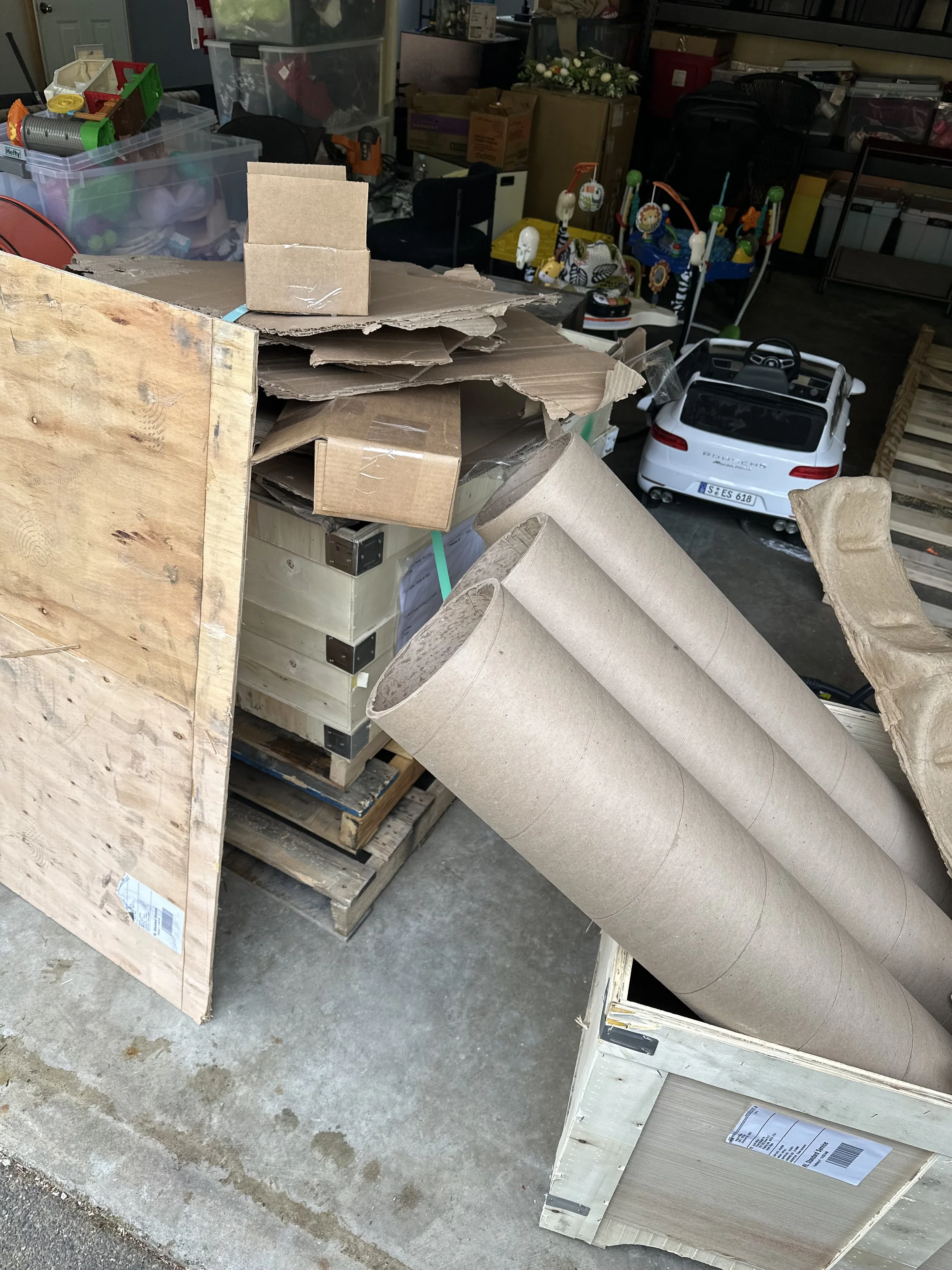 Pile of scrap lumber and wood boards beside stacked shipping boxes and storage items inside a Puyallup garage.