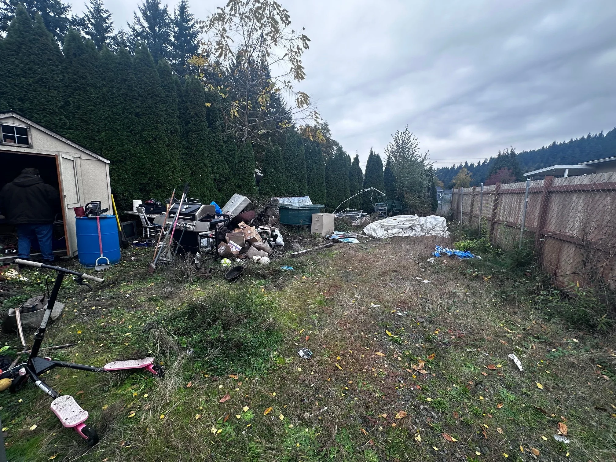 Before — wide view showing sheds, tarps, and trash piled along the fence.