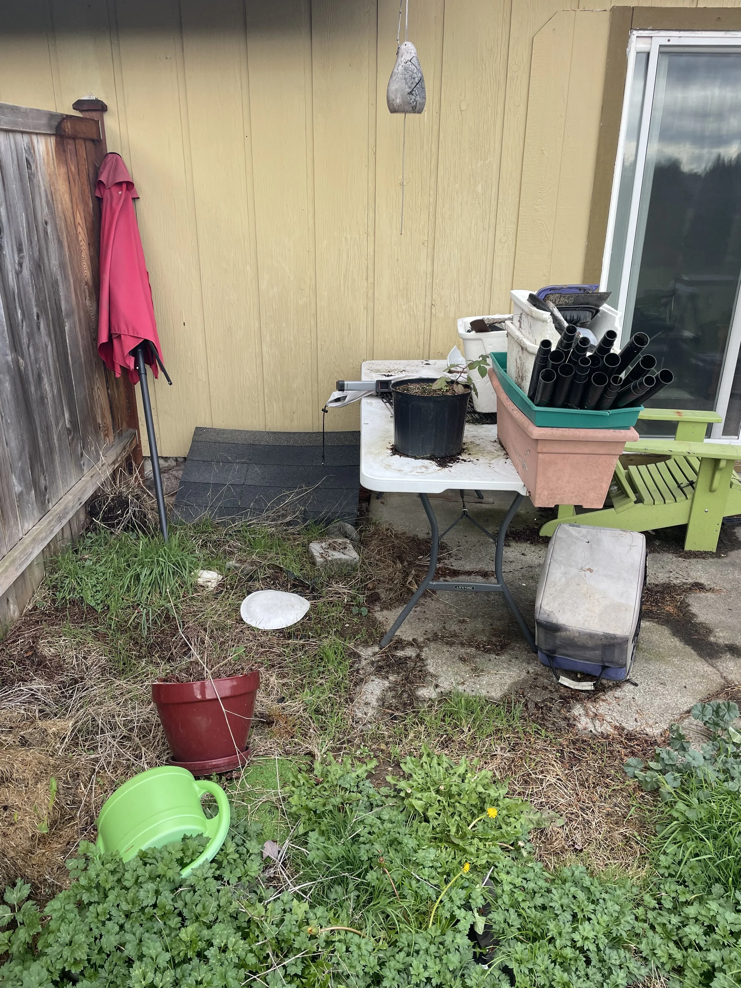 Back patio cluttered with old planters, pipes, garden supplies, and yard debris before clean-out.
