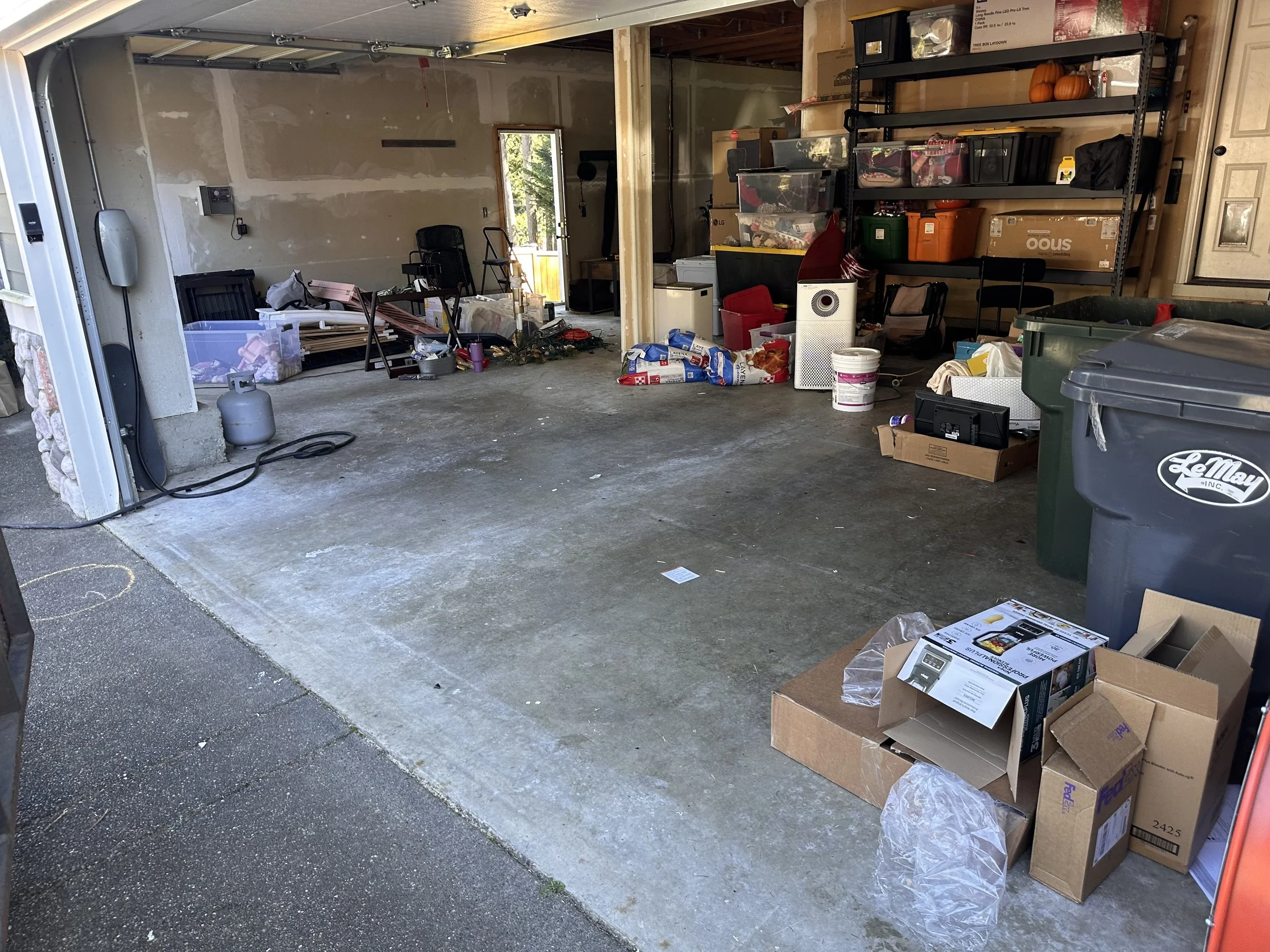Residential garage with open concrete floor space after bulky wood debris removal, with shelving and stored belongings remaining.