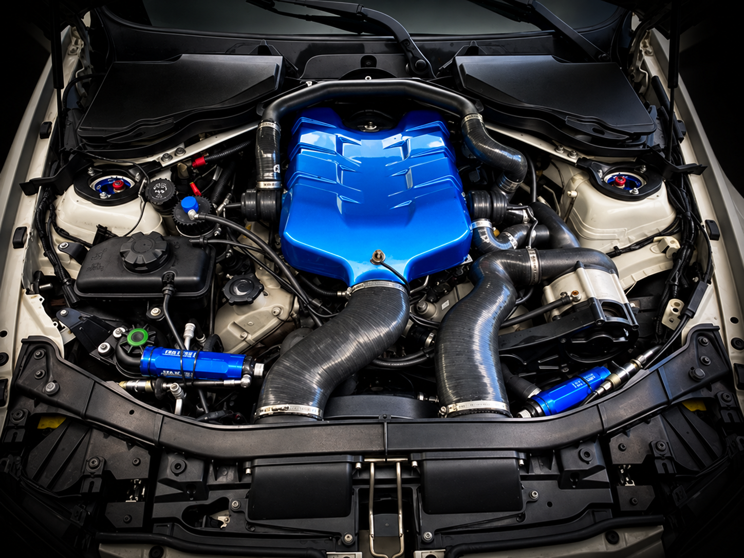 Under the hood of a car showing a blue engine cover and various engine components, hoses, and wiring.