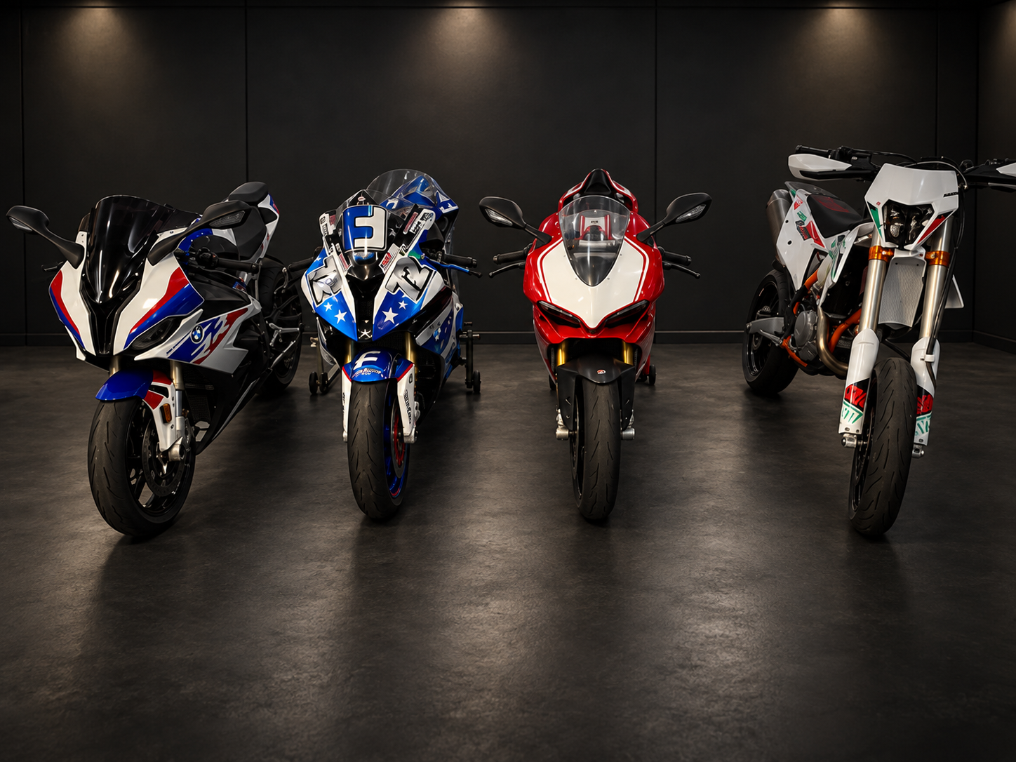 Four high-performance motorcycles parked side by side in a garage, with a metallic garage door in the background and various gear to the right.