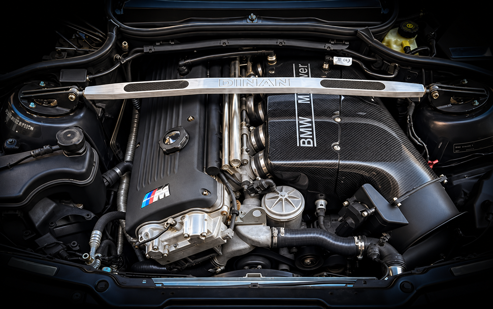 Close-up of a BMW car engine with a metallic brace labeled 'Dinan' spanning across it.