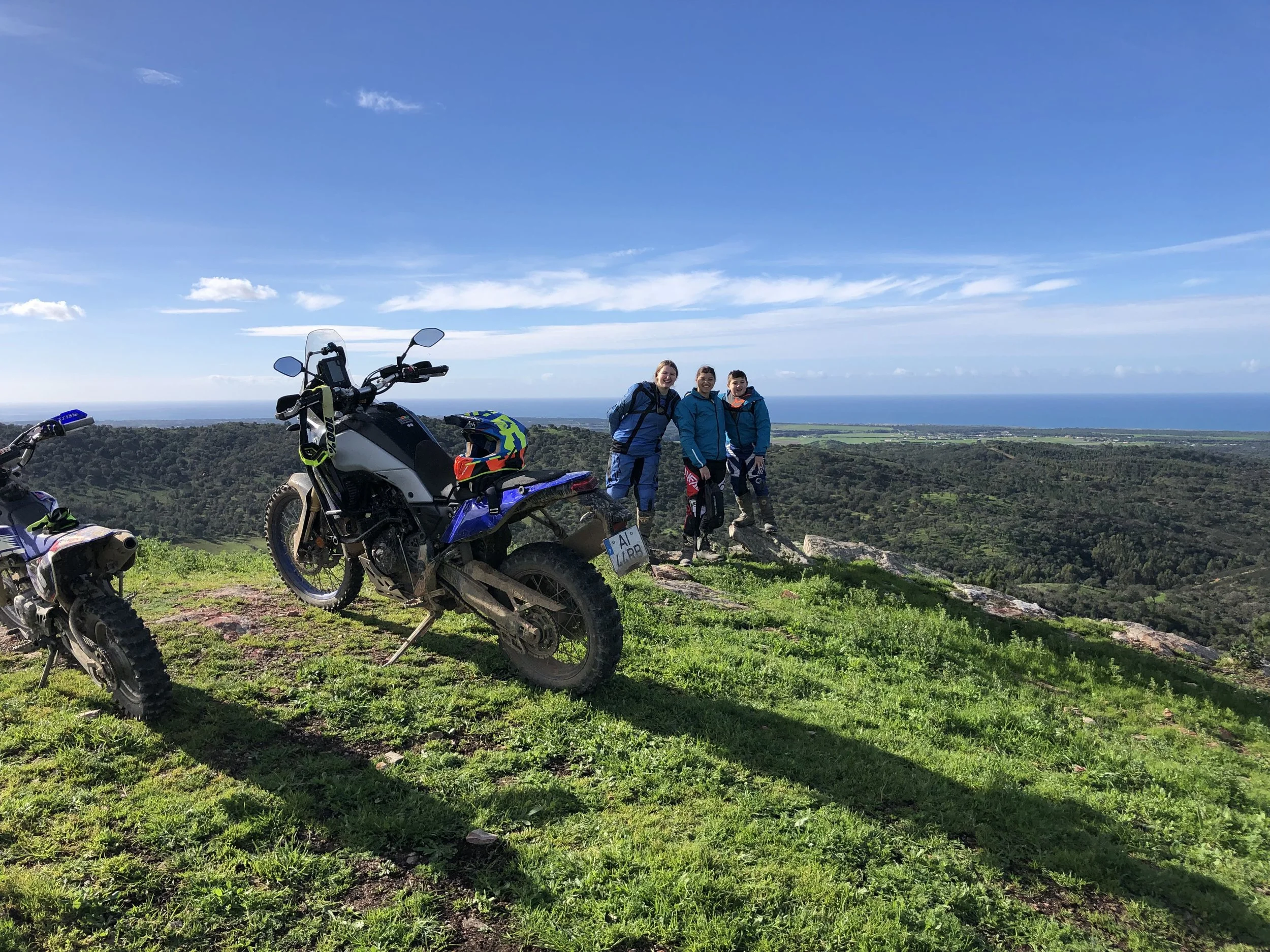 Adventure motorcycle and riders on a green hilltop above the sea in Portugal