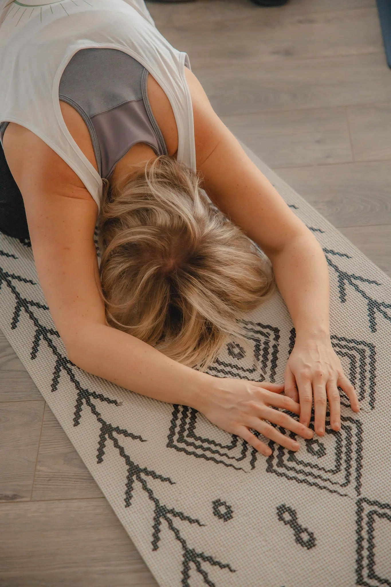 Two women practicing yoga in a studio, one in a downward-facing dog pose and the other in a side stretch pose, with a decorated wall and plants in the background.