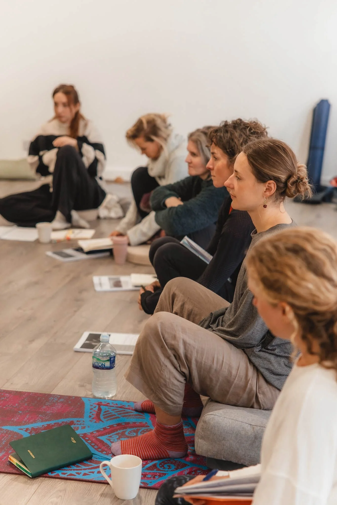 People sitting on the floor with notebooks, books, and drinks, participating in a class or workshop.