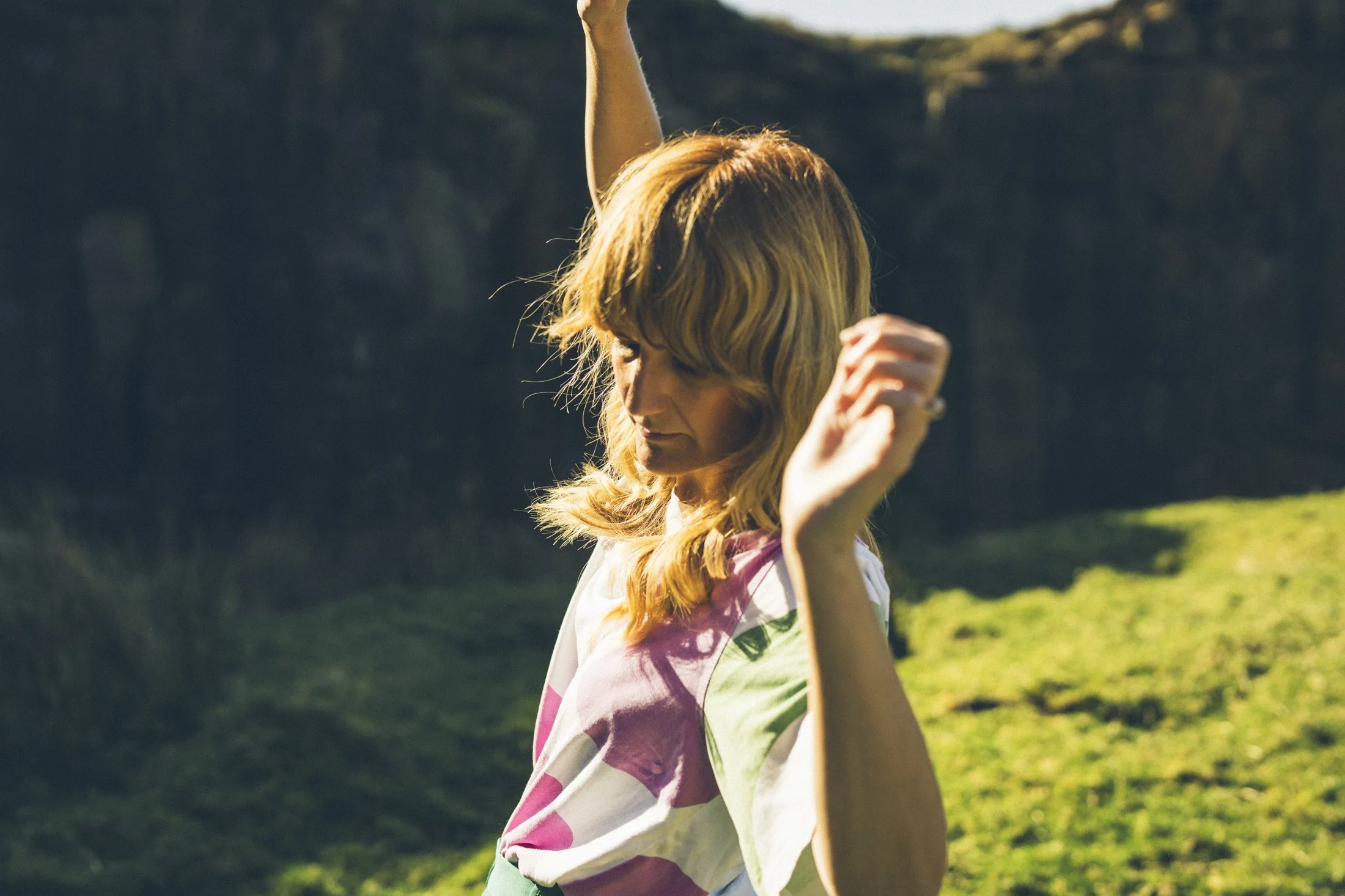 A woman with blonde hair dancing outdoors in a grassy area during sunset or late afternoon.
