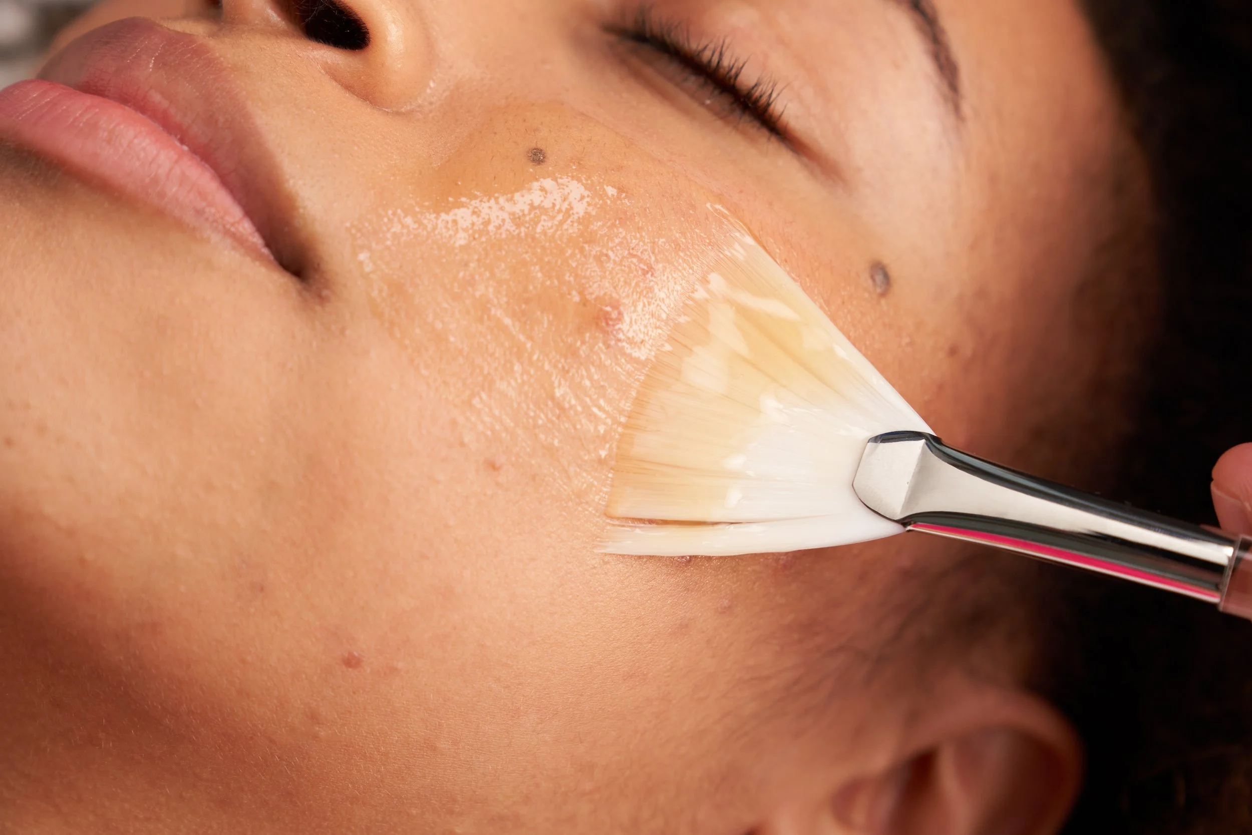 Close-up of a person receiving a facial treatment with a brush applying a cream or mask to their face.