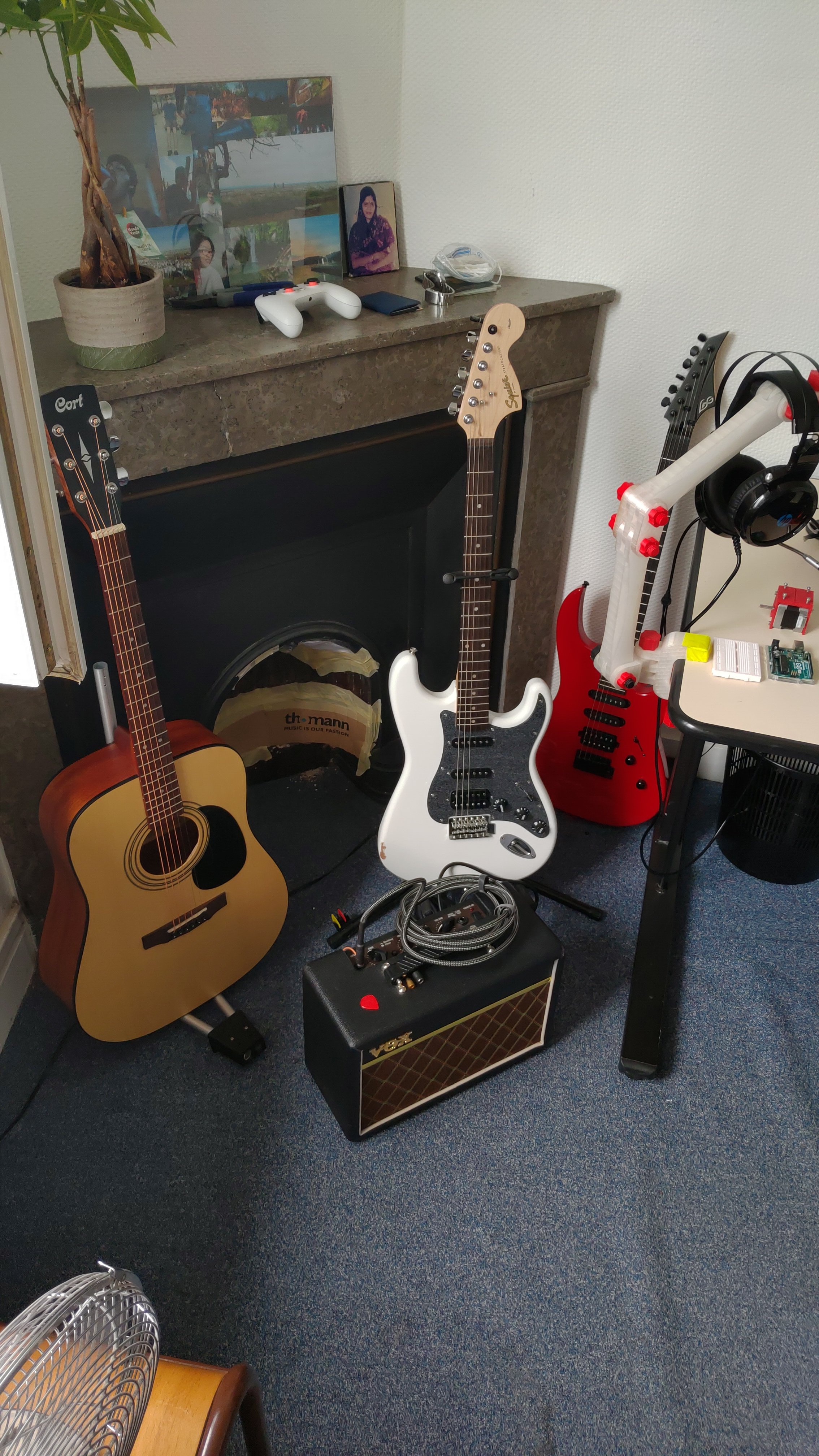 Room with two guitars, a guitar amplifier, and a music stand, with a computer and headphones on a desk nearby.