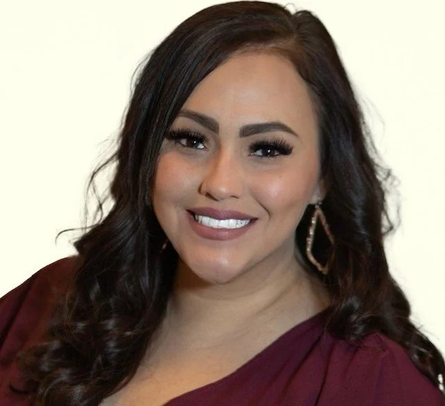Smiling woman with long brown hair wearing earrings and a red top.