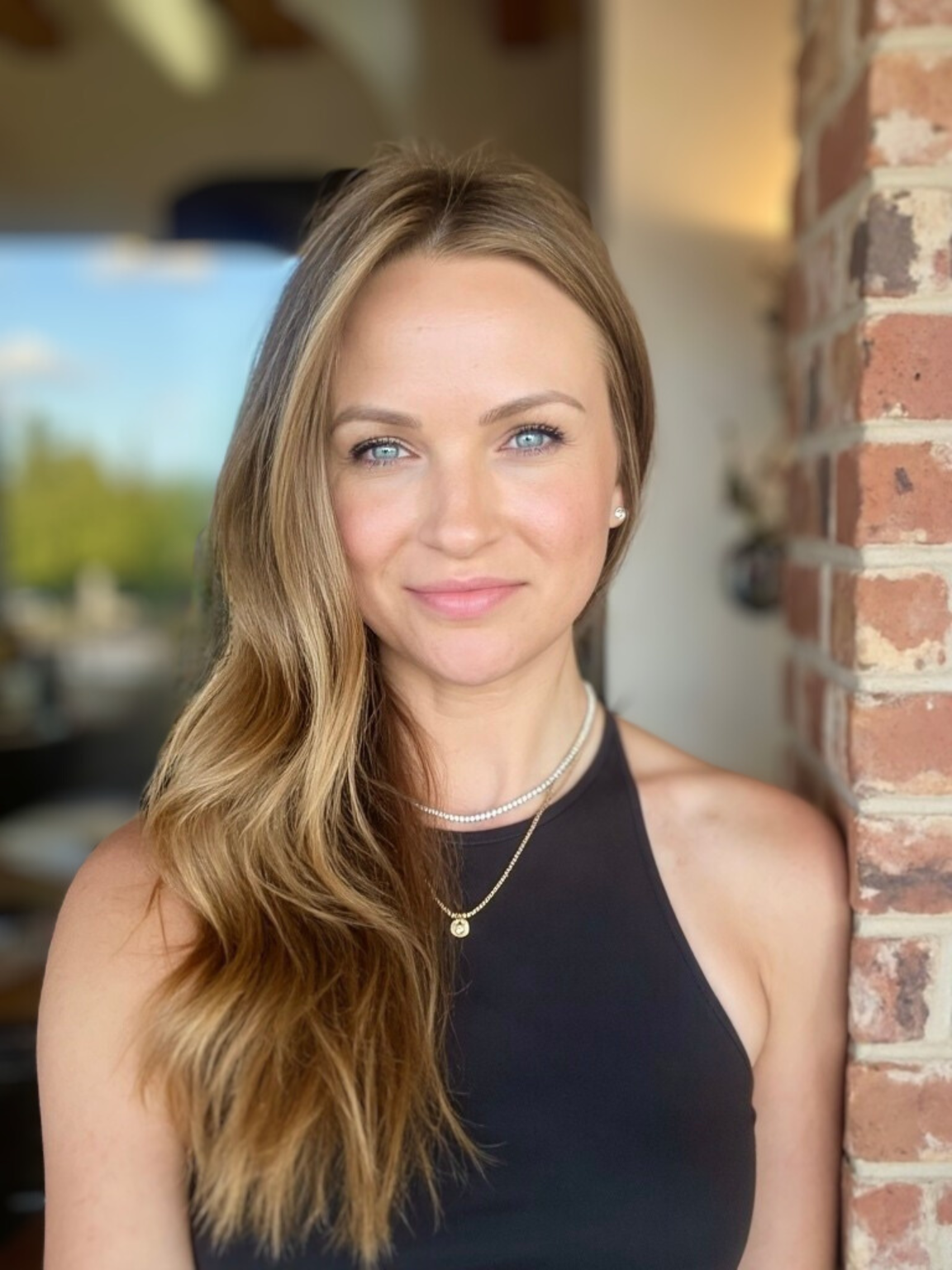 Woman with long hair in a blue blouse smiling against a brown background.