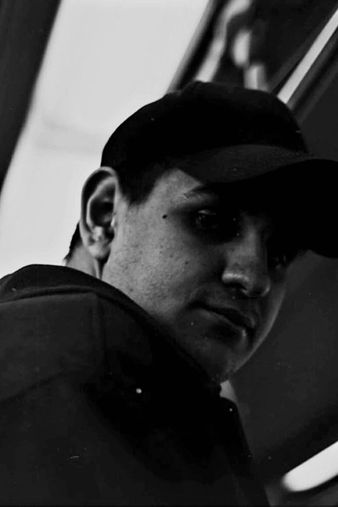 Black and white photo of a person wearing a cap and looking slightly to the side.