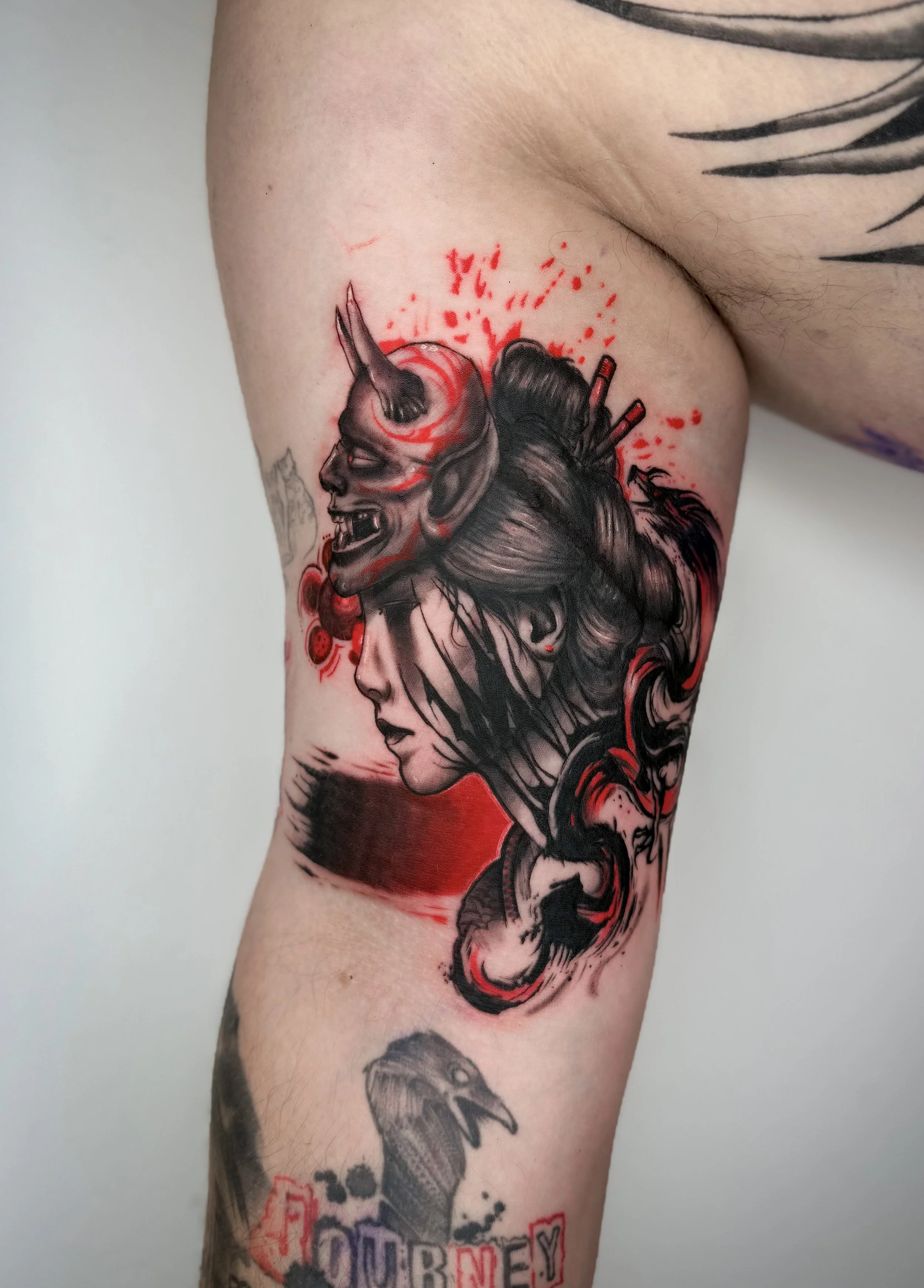 Japanische Frau mit Hannya-Maske als Black-and-Grey-Tattoo mit roten Akzenten und abstrakten Elementen, tätowiert auf der Innenseite des Oberarms.