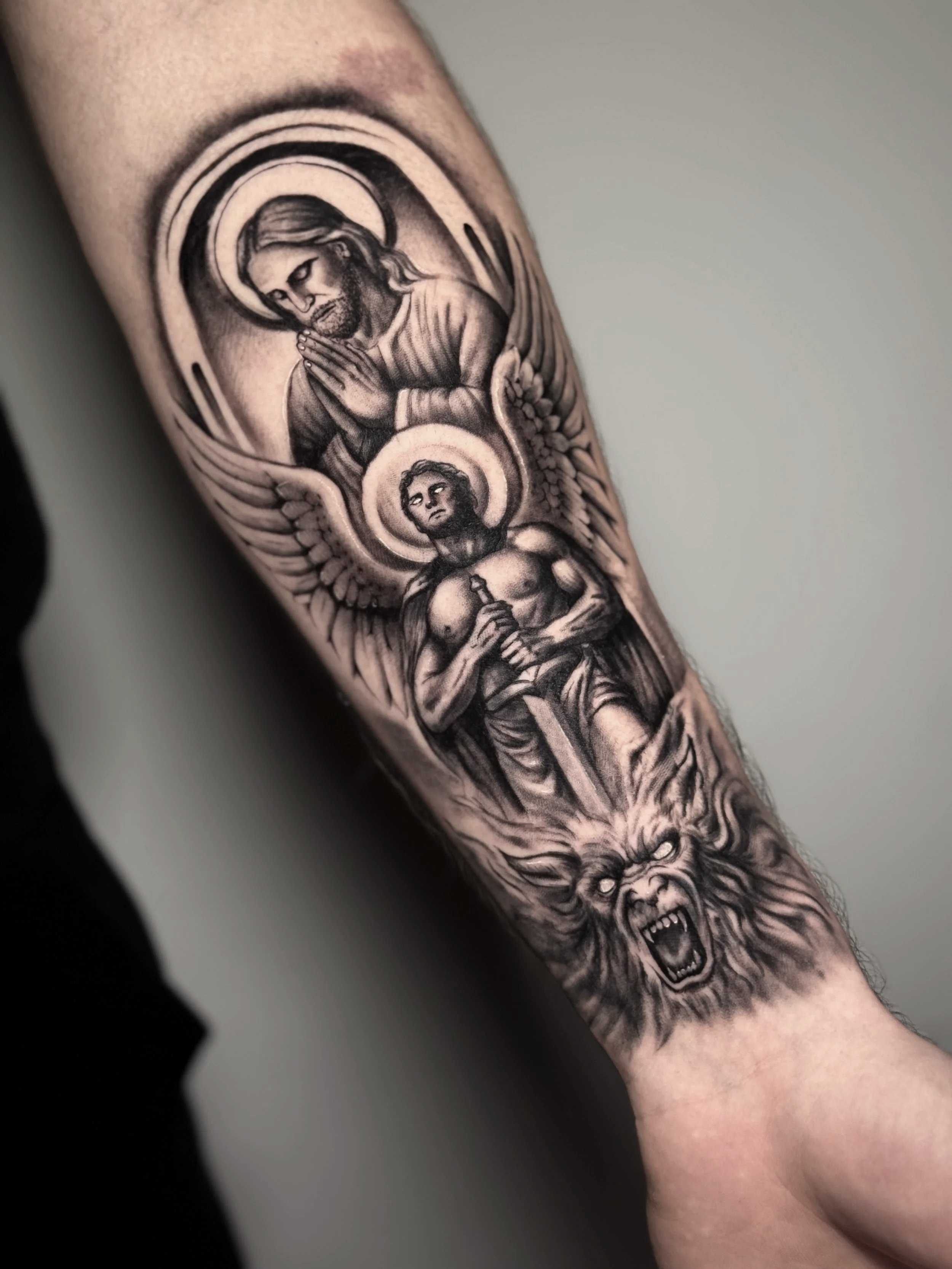 Realistisches Black-and-Grey-Unterarmtattoo mit Jesus, einem Engel und einem besiegten Dämon.