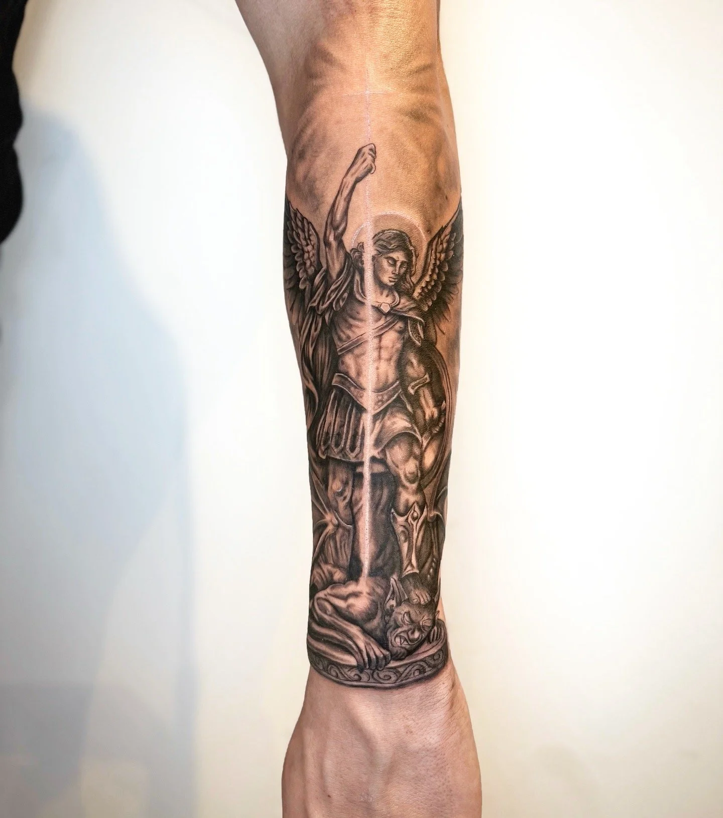 Black-and-Grey-Realistic-Tattoo eines Erzengels auf dem Unterarm, mit fein ausgearbeiteten Details und dynamischer Lichtführung.