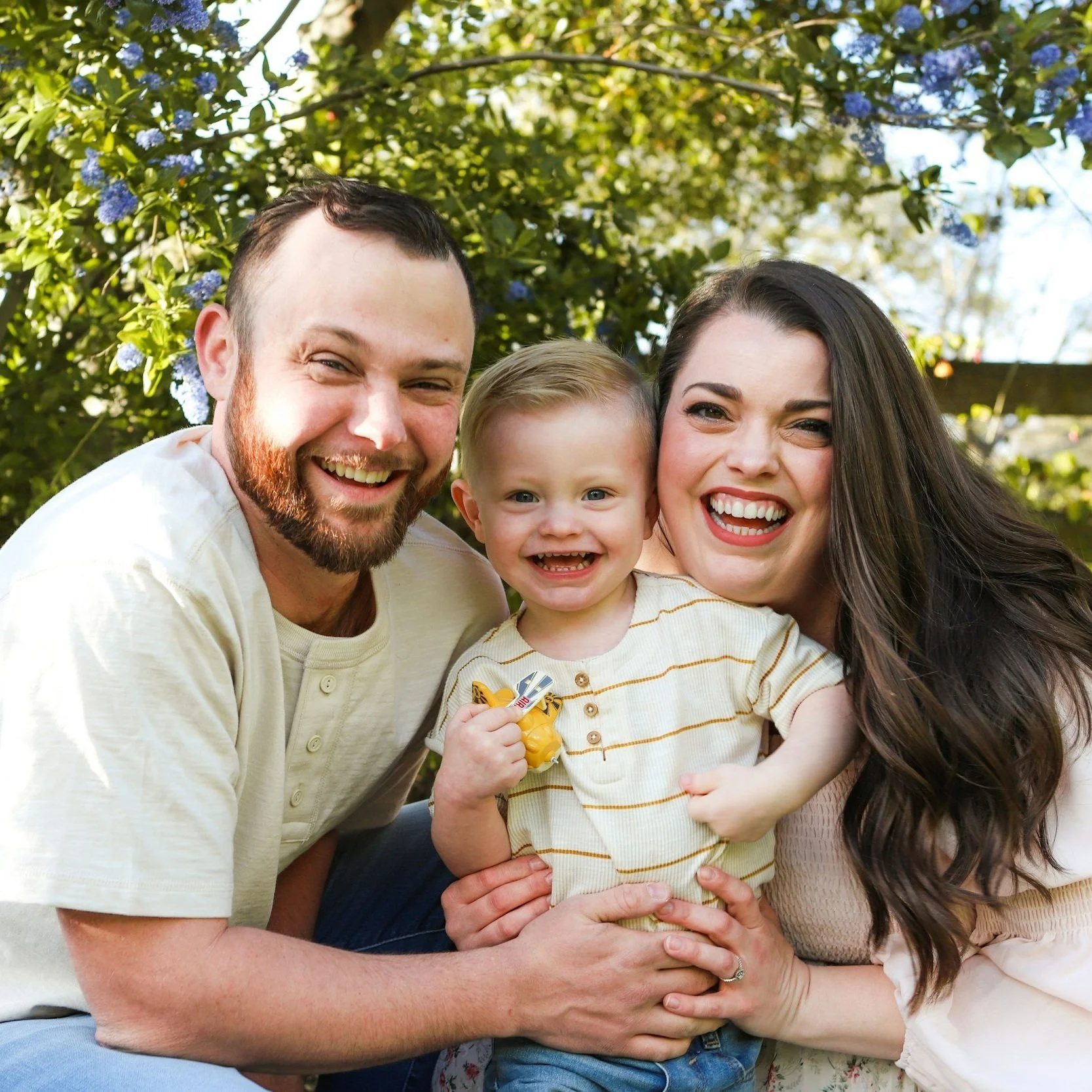 Smiling family of three with trees in background