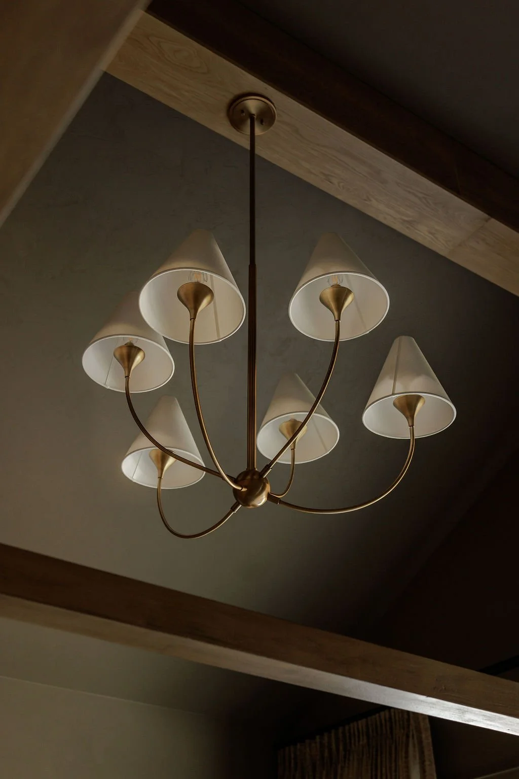 A chandelier with seven curved arms, each holding a white conical lampshade, hanging from a ceiling.