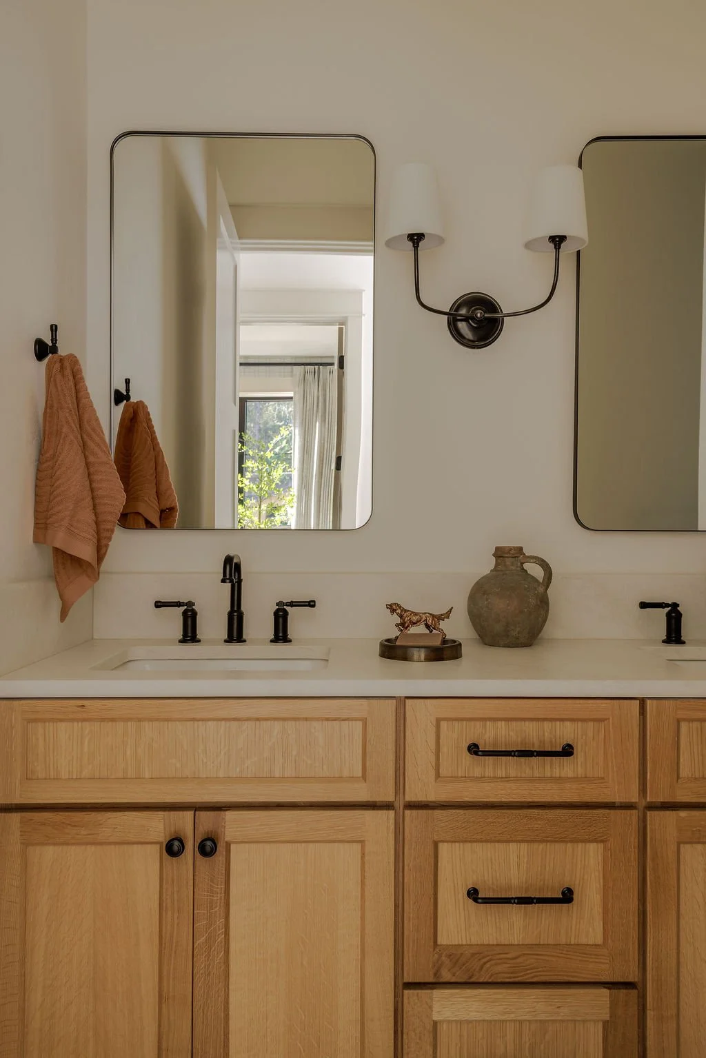 A bathroom vanity with two mirrors, a light fixture, and decorative items including a small sculpture of a tiger and a rustic clay pitcher.
