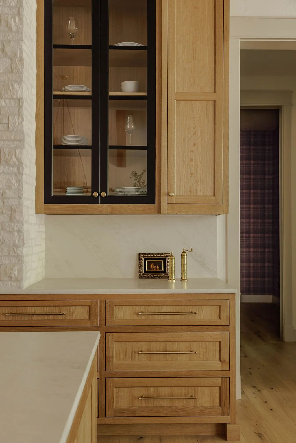 Kitchen with wooden cabinets, glass-front upper cabinet, white countertops, and a small decorative picture frame with gold fixtures on the counter.