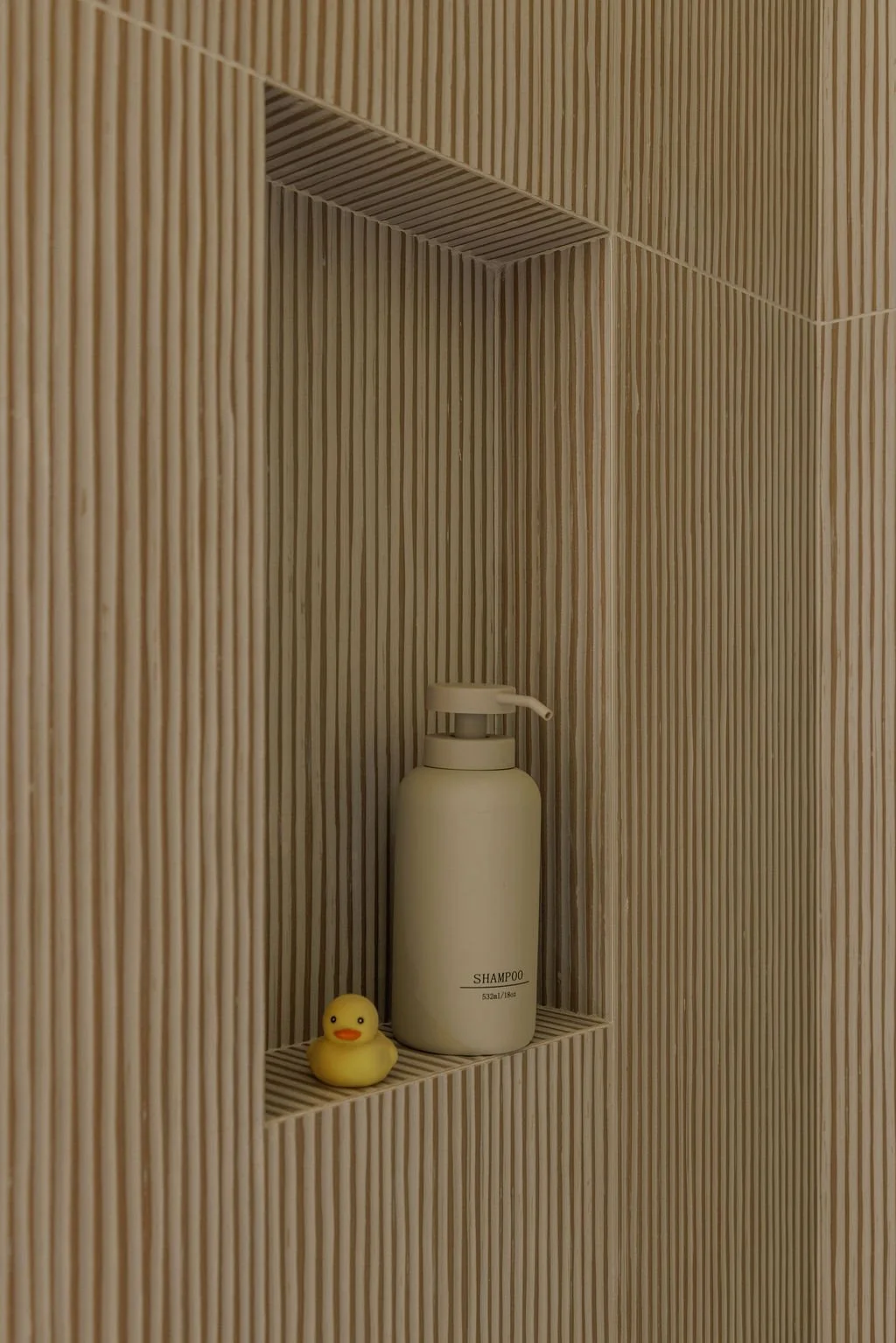 A bamboo wall shelf in a shower with a white shampoo bottle and a yellow rubber duck.