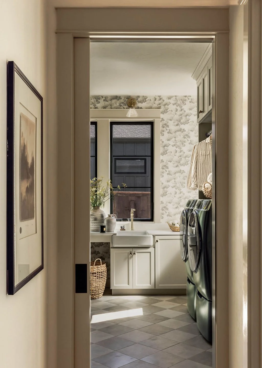 View through doorway into a laundry room with white cabinetry, a window, washer and dryer, and decorative items.