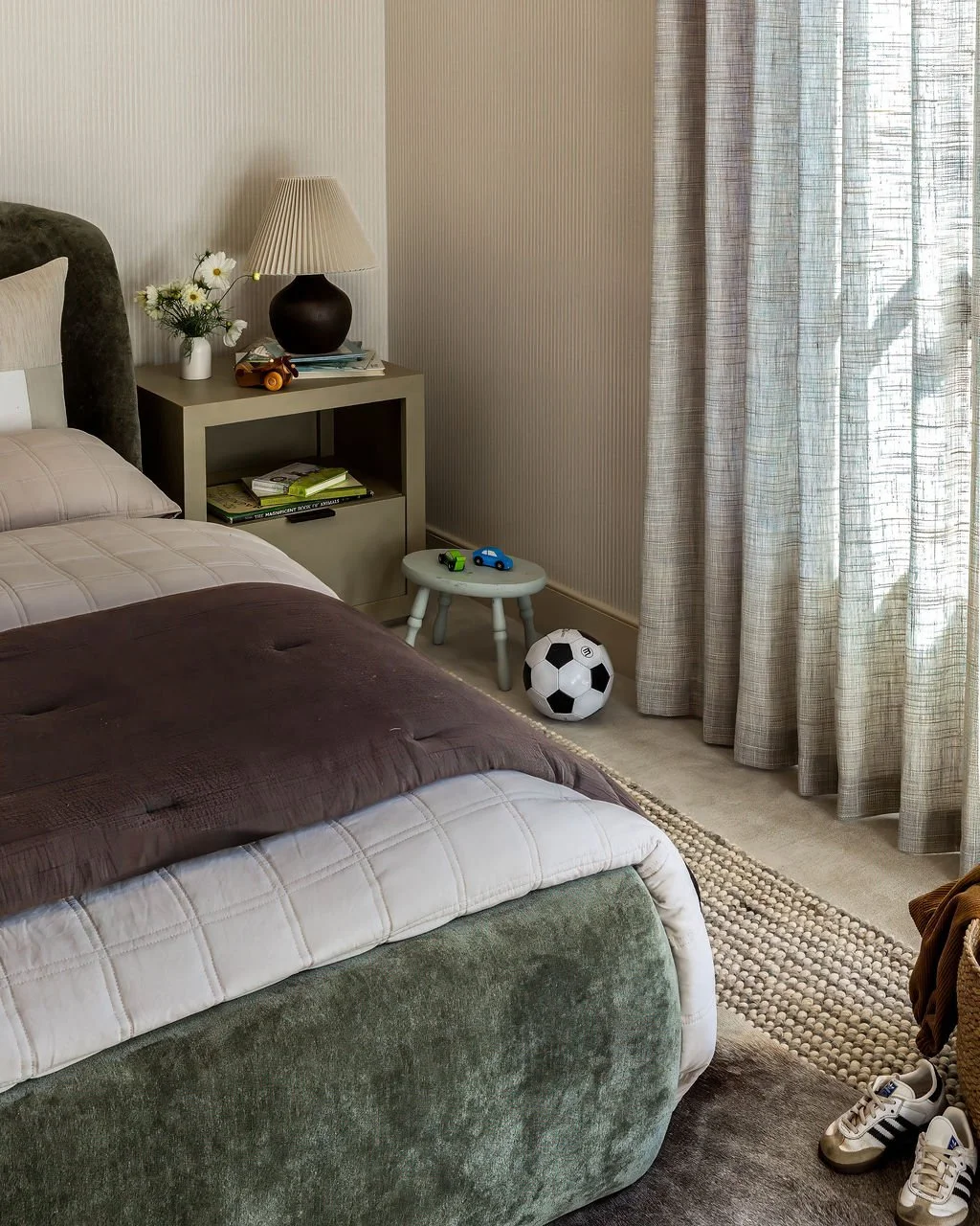 Bedroom corner with bed, nightstand, toys, soccer ball, and curtains.