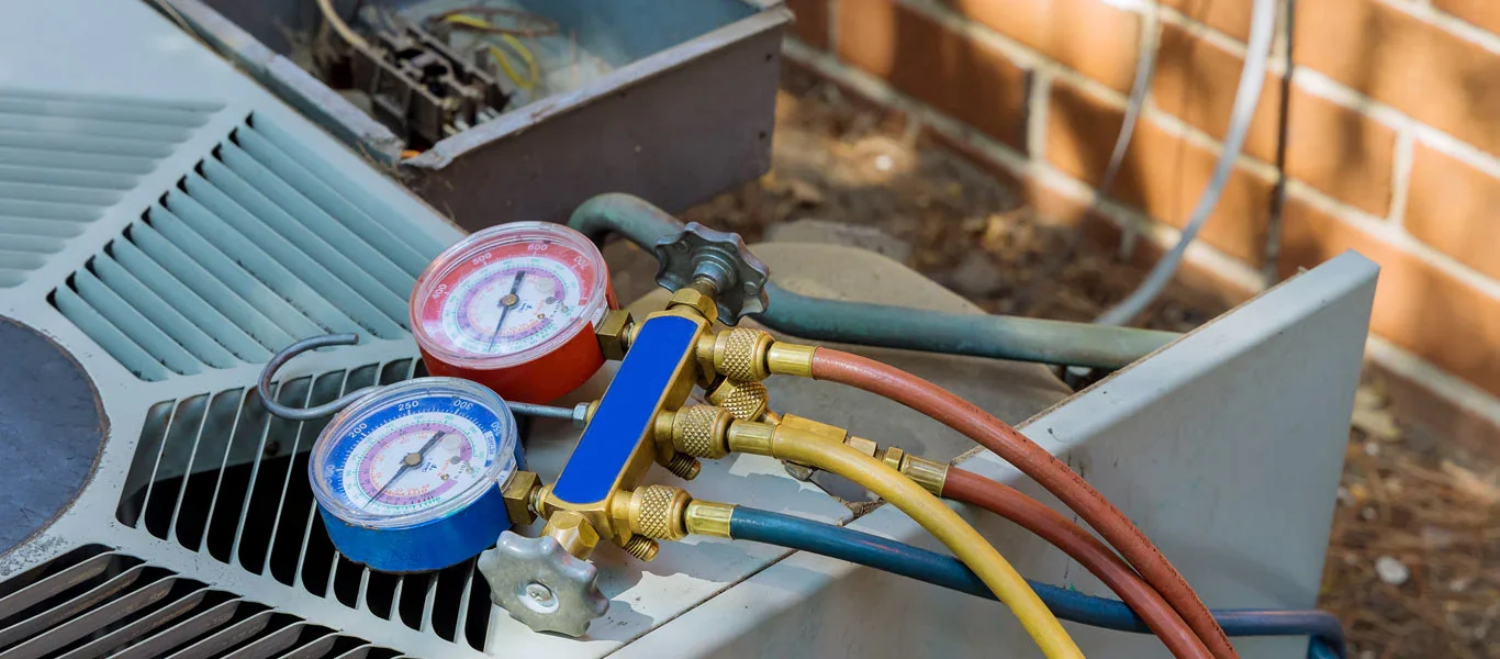 HVAC gauges connected to an outdoor air conditioner condenser to measure refrigerant pressure during AC system diagnostics