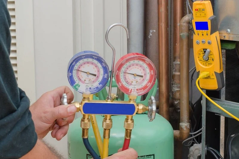HVAC technician checking refrigerant pressure gauges during air conditioner spring maintenance