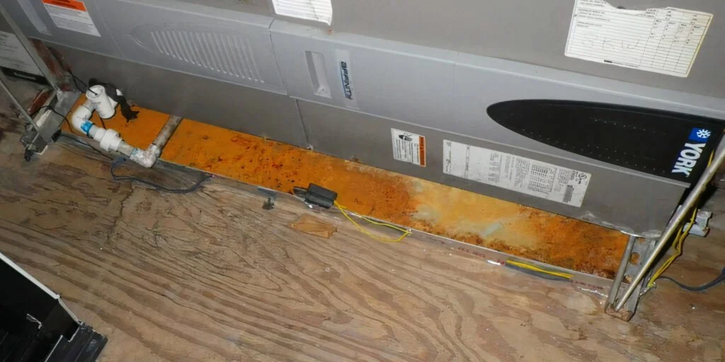 severely rusted AC drain pan beneath a York air handler with water damage on surrounding subfloor
