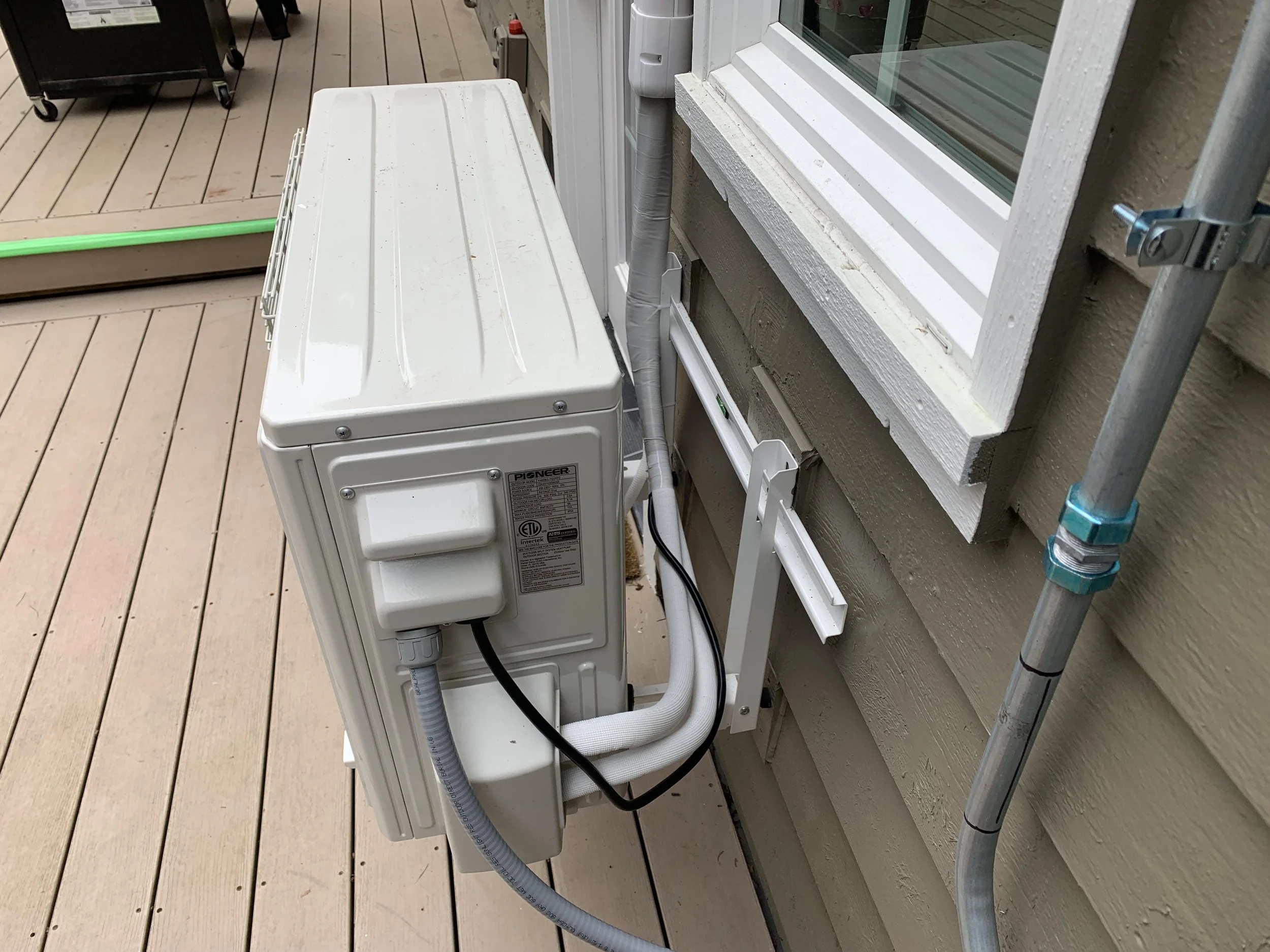 Pioneer mini split outdoor condenser unit mounted beside a window with insulated refrigerant line set in Orange County home
