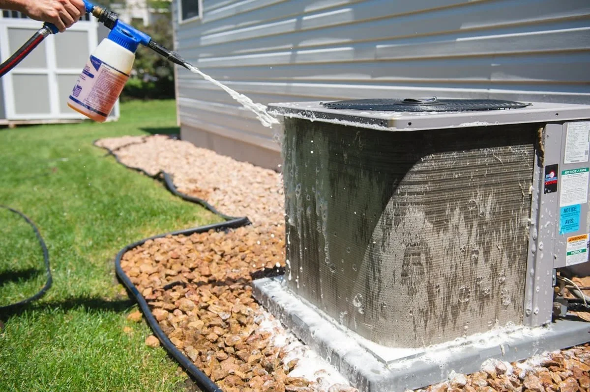 Cleaning outdoor air conditioner condenser coils with water during spring HVAC maintenance