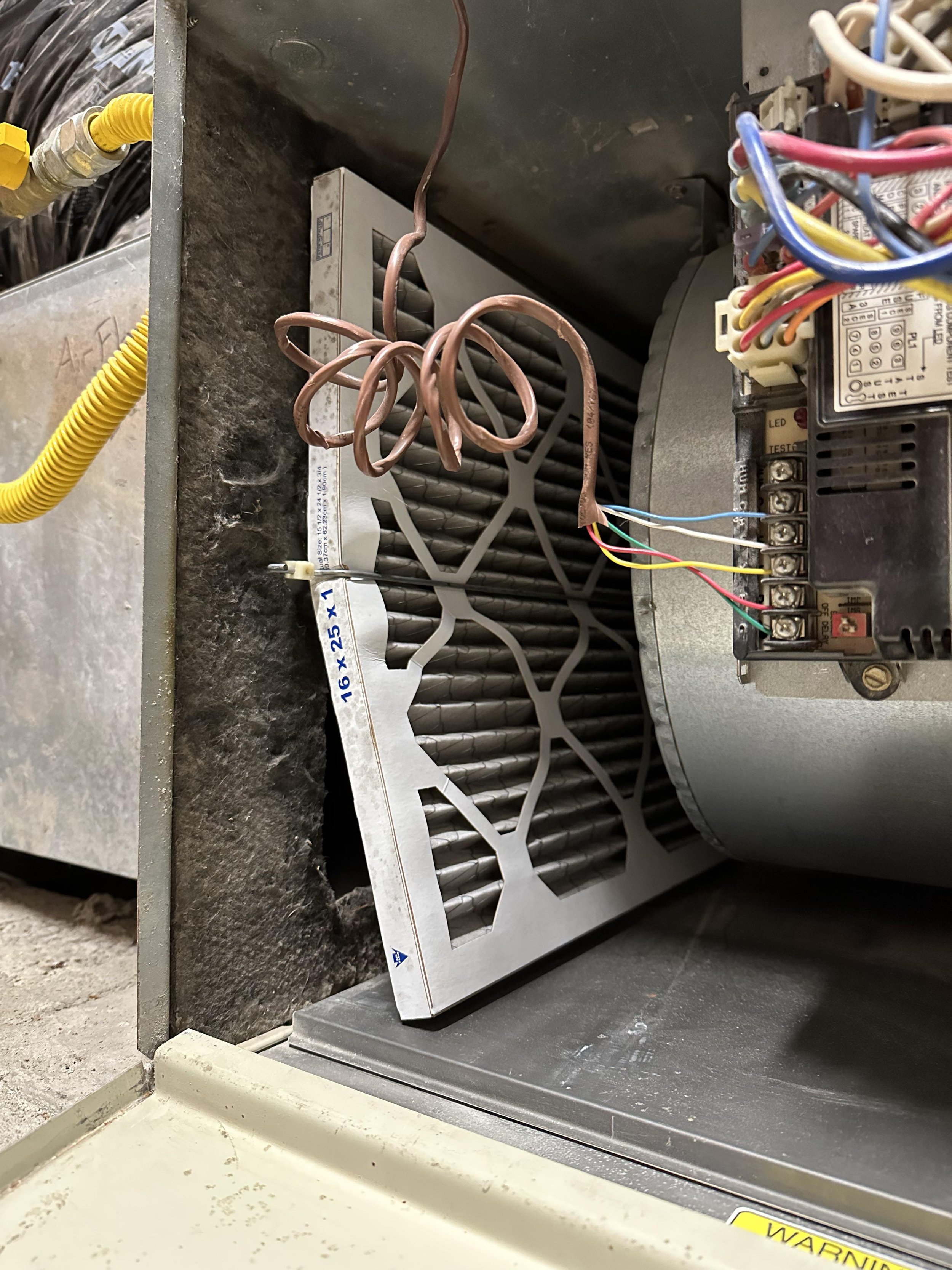 heavily loaded and bent 16x25x1 pleated AC filter partially removed from an Orange County air handler unit