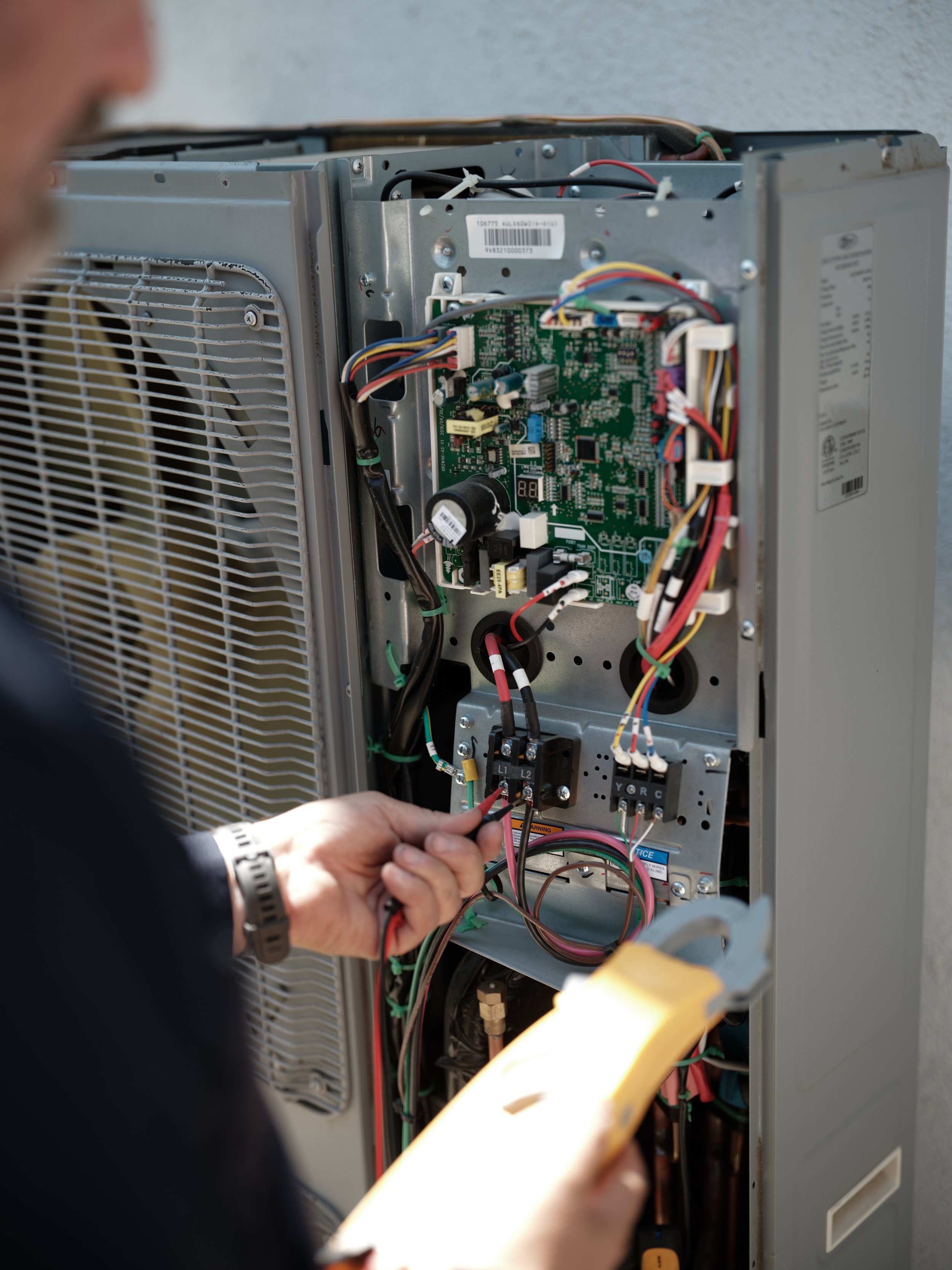 technician inspecting wiring and electrical connections inside air conditioning unit