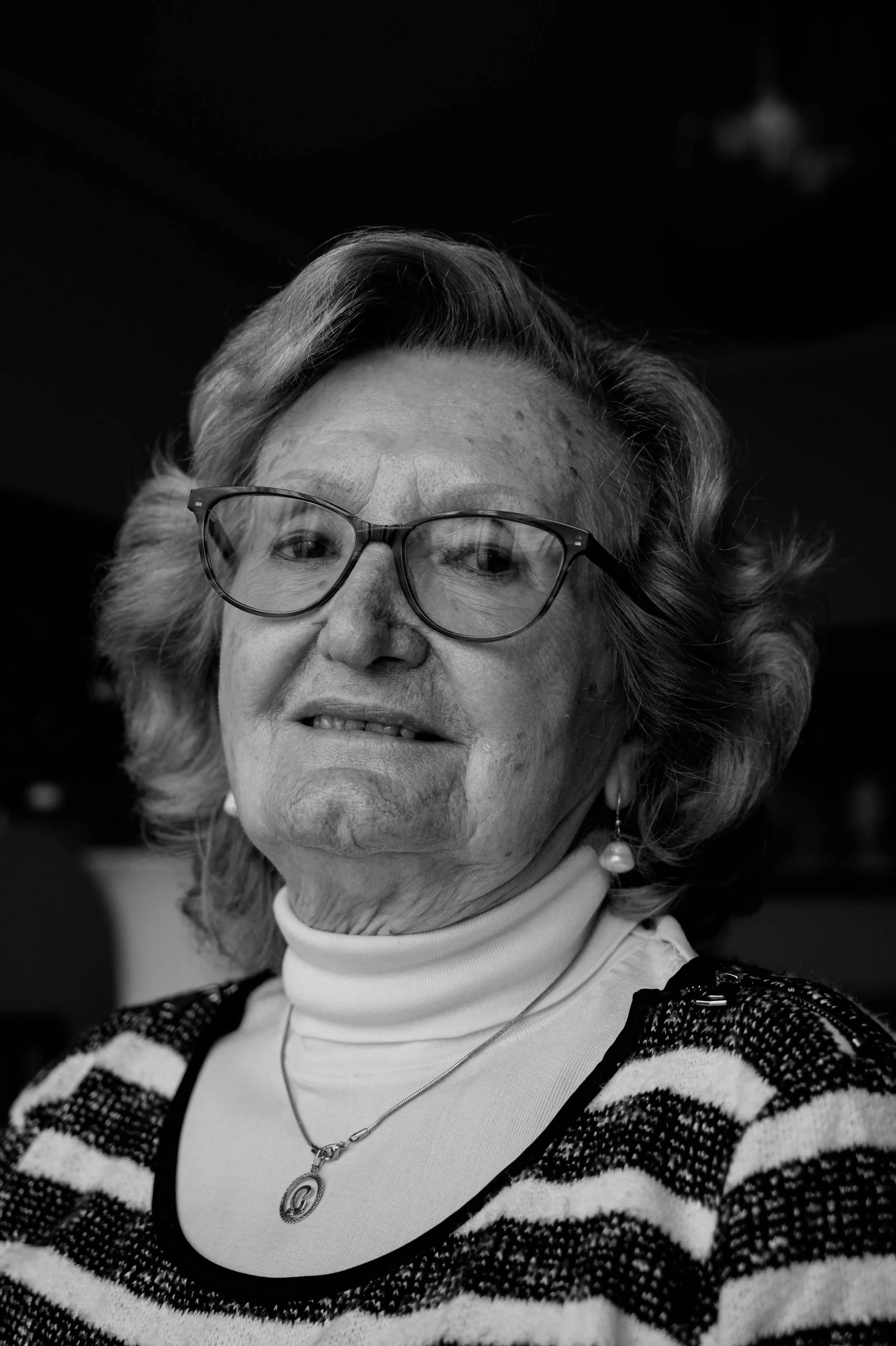 A woman with short, light brown hair and glasses smiling at a restaurant table with a drink and menu in front of her.