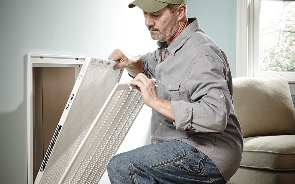 man inspecting a Honeywell disposable pleated AC filter removed from a wall return air vent