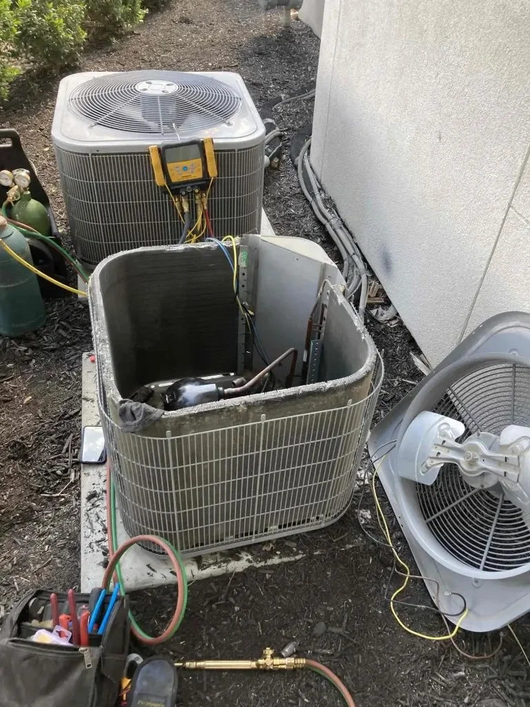 AC compressor not working diagnosis in Orange County, with refrigerant gauges and recovery equipment connected to an outdoor condenser unit during repair or replacement evaluation
