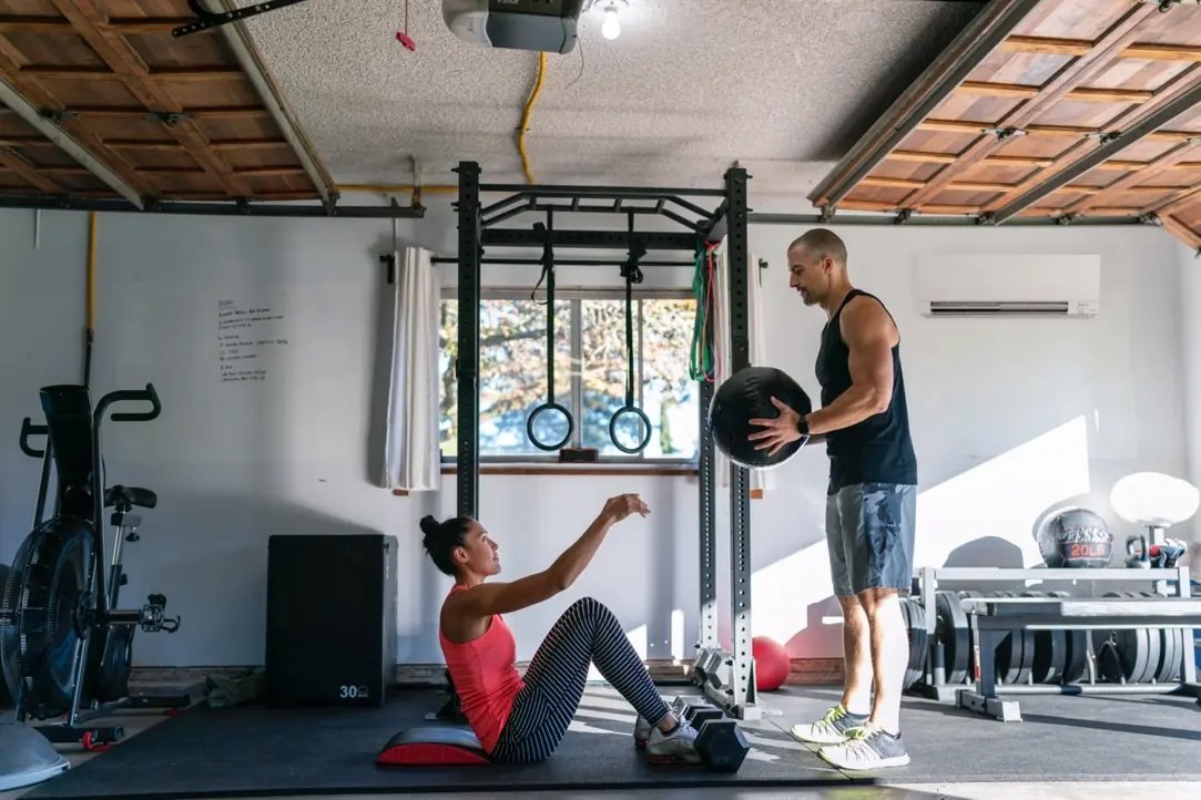 Two people working out in a converted garage home gym with a mini split wall unit mounted in the upper right corner