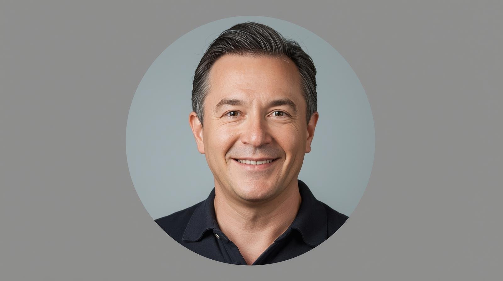 A man with crossed arms standing in front of colorful blooming flowers in a park, with people and buildings in the background.