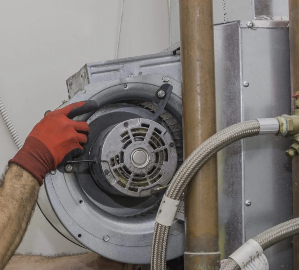 HVAC technician inspecting an indoor blower motor inside a residential air handler to diagnose airflow problems that can lead to a frozen evaporator coil