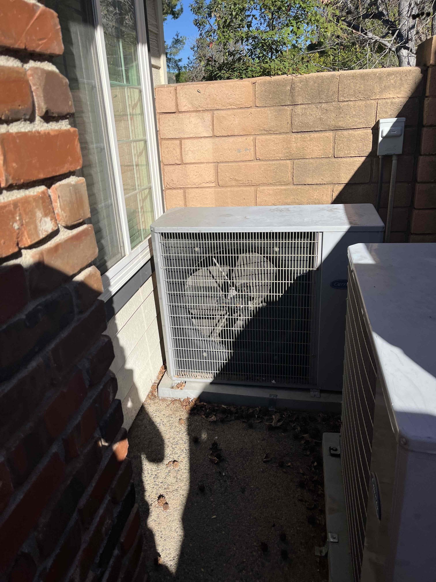 outdoor AC condenser unit with leaf debris buildup in residential side yard requiring maintenance service in Orange County