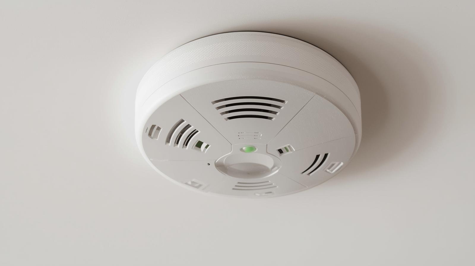 Carbon monoxide detector on ceiling with green indicator light showing proper function for home safety