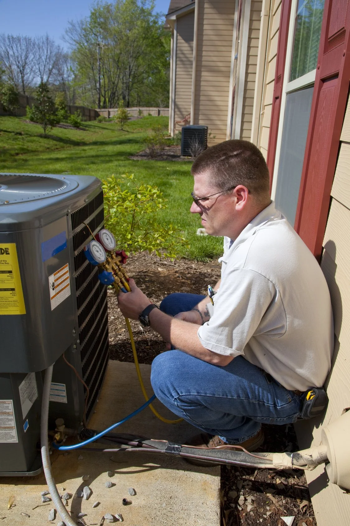 HVAC technician inspecting an outdoor residential air conditioner condenser unit