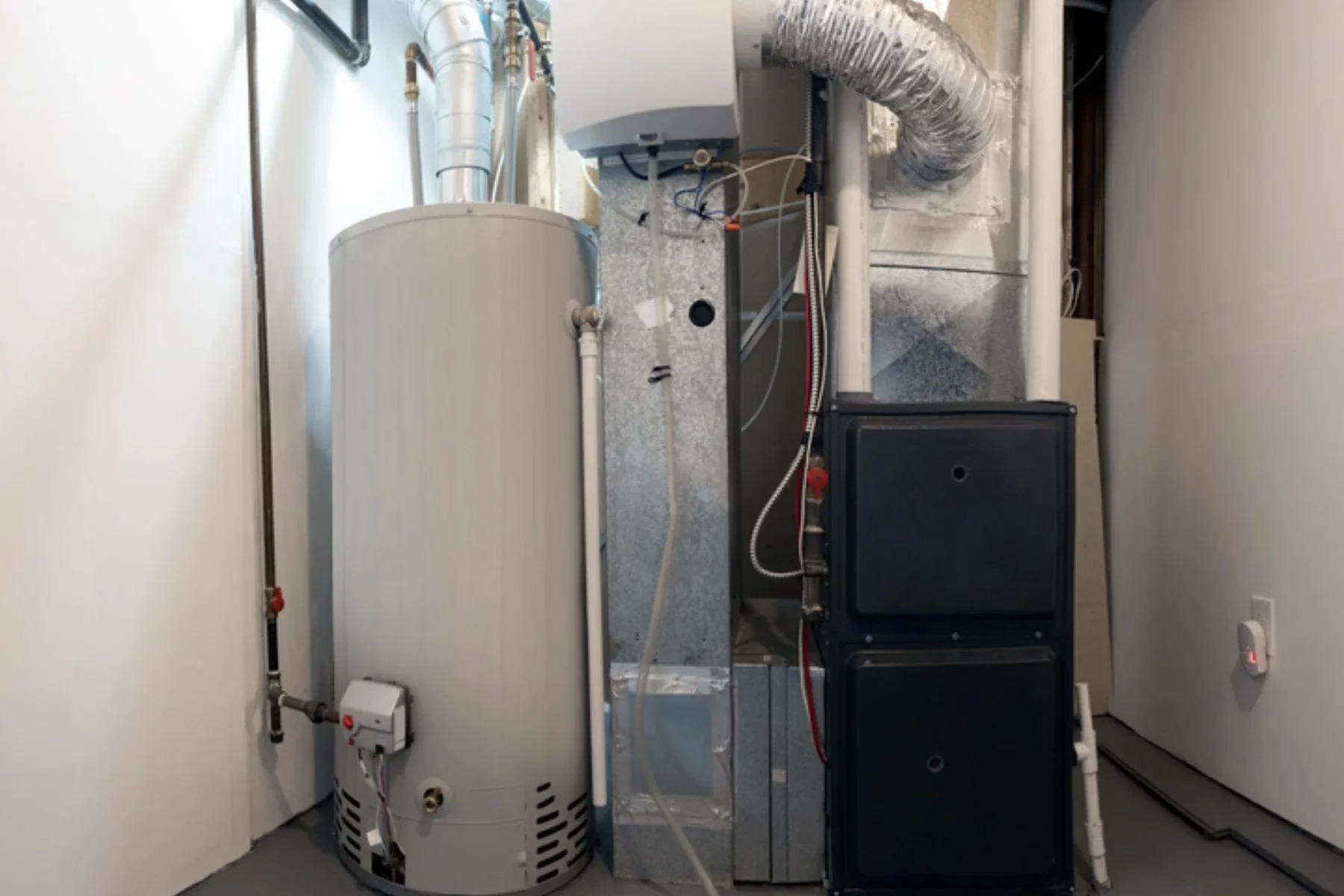 gas furnace and water heater installed side by side in a tight residential closet, showing ductwork, gas lines, and electrical wiring in an Orange County home
