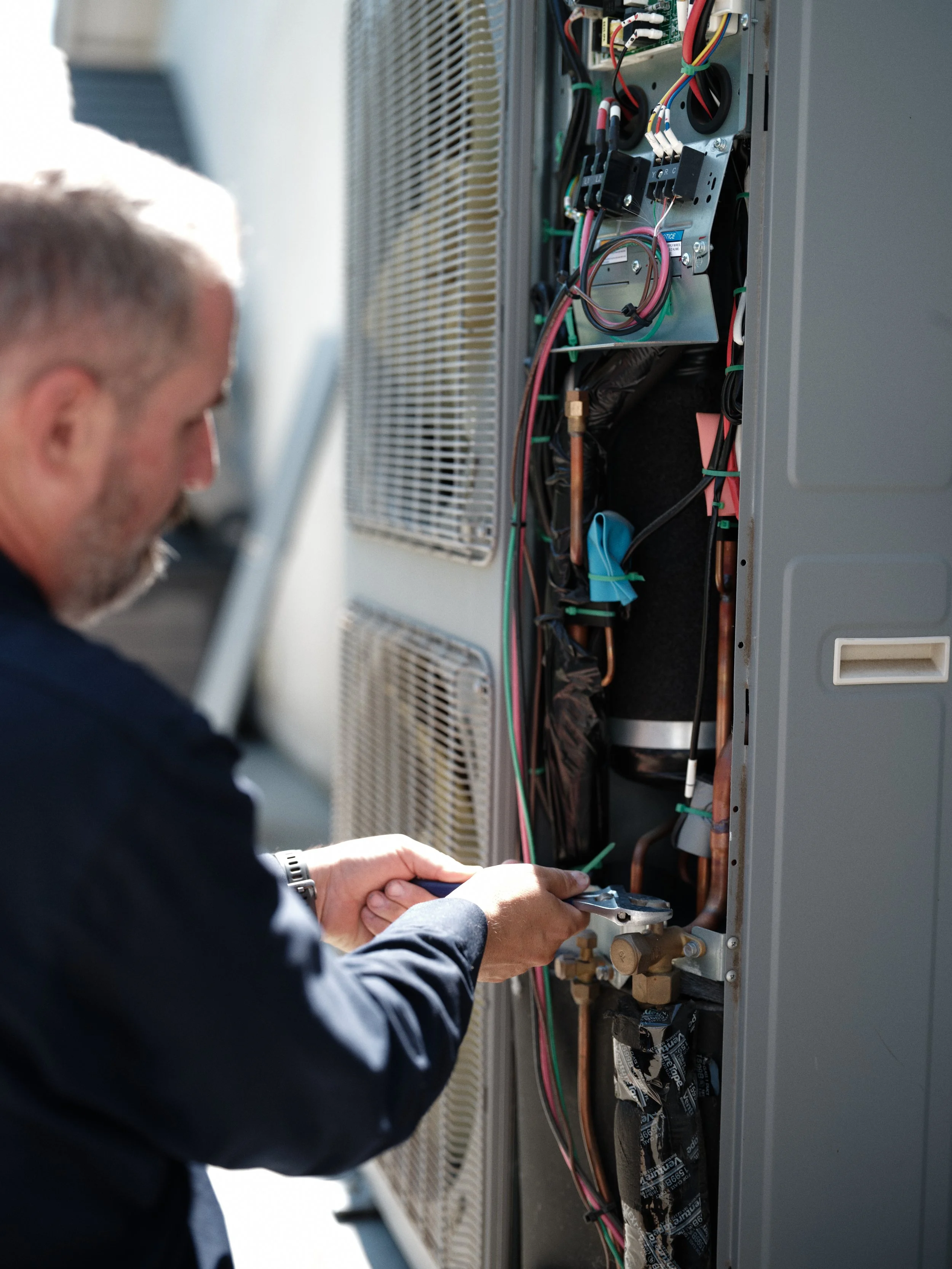 J Martin HVAC technician evaluating outdoor unit condition to help Orange County homeowner make informed heating and cooling replacement decision